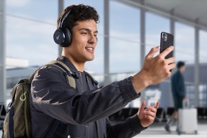 A man in an airport looking at a phone while wearing the Anker Space One headphones.