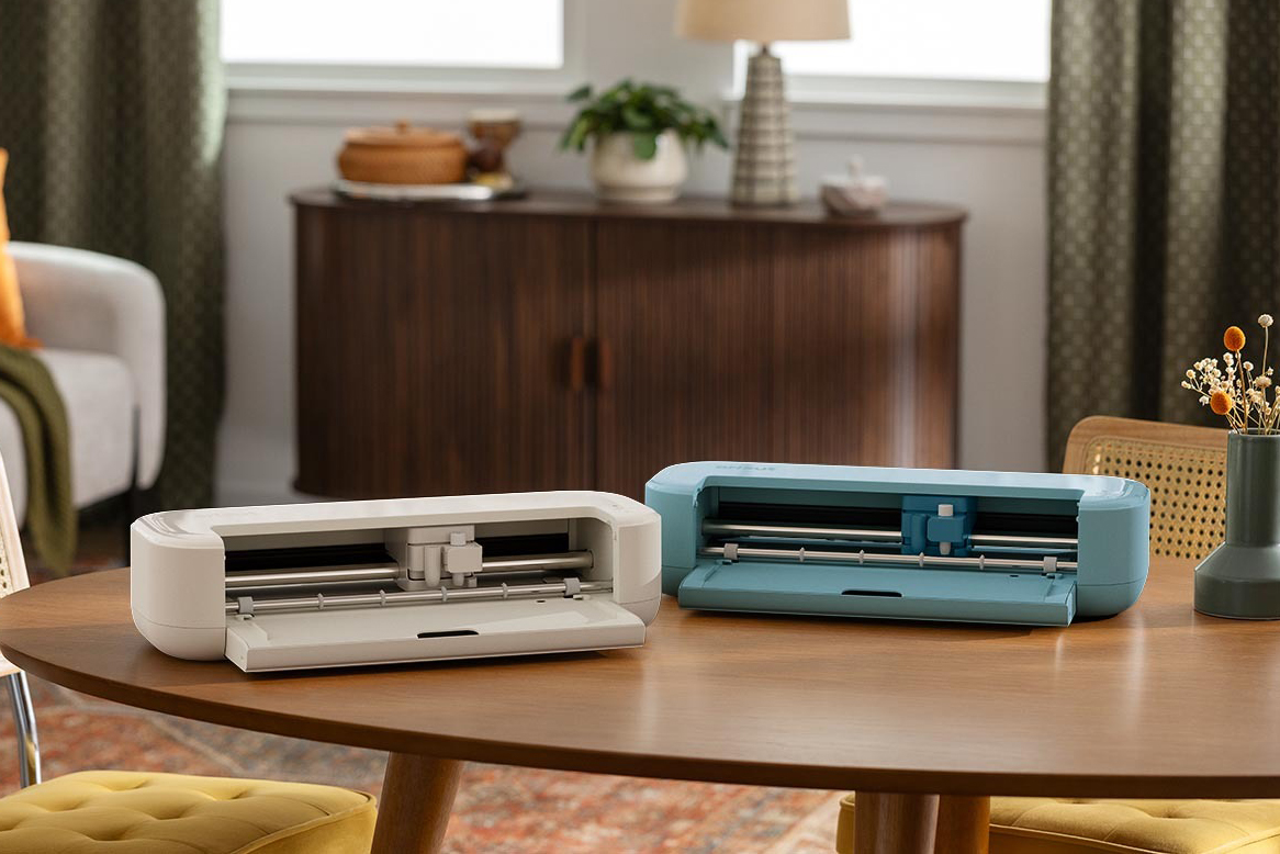 Two Cricut Explore 5 machines in different colors sitting on a table.