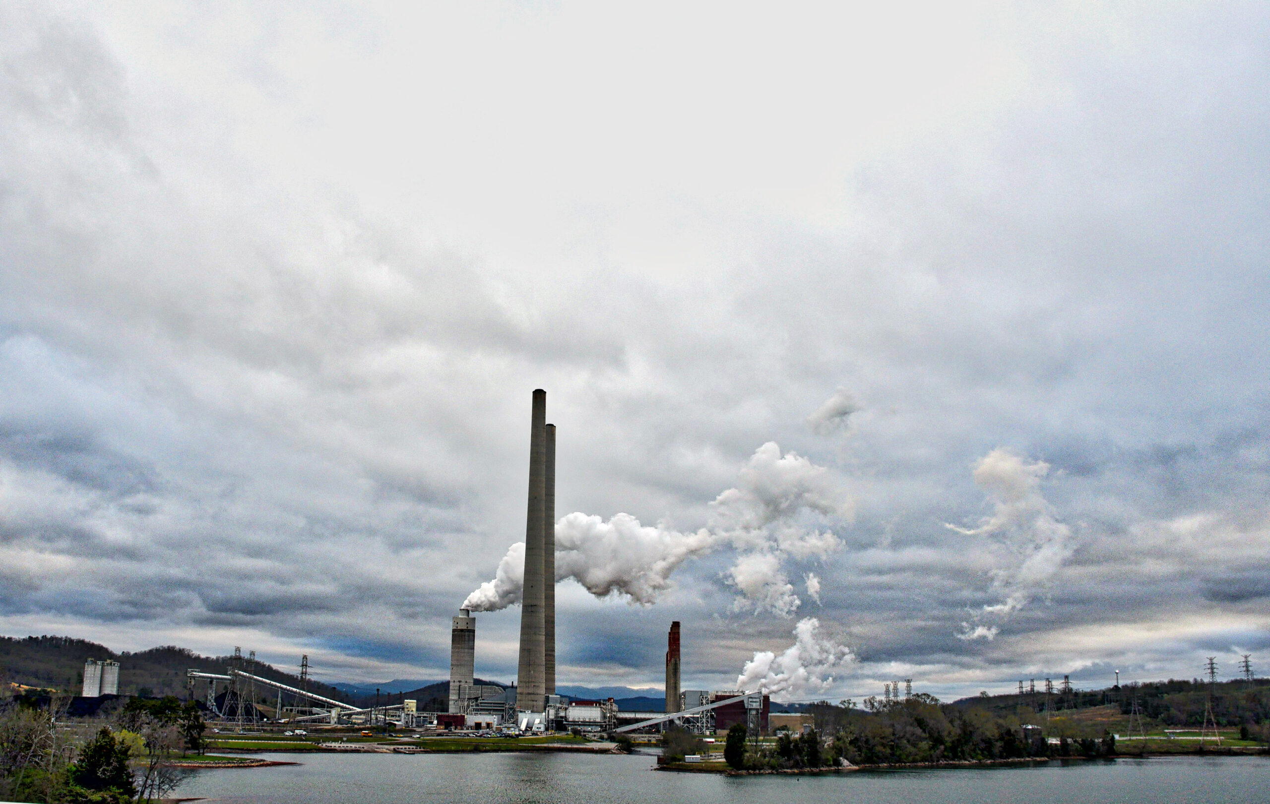 A photo of emissions rising from coal plant along a lake shore. 