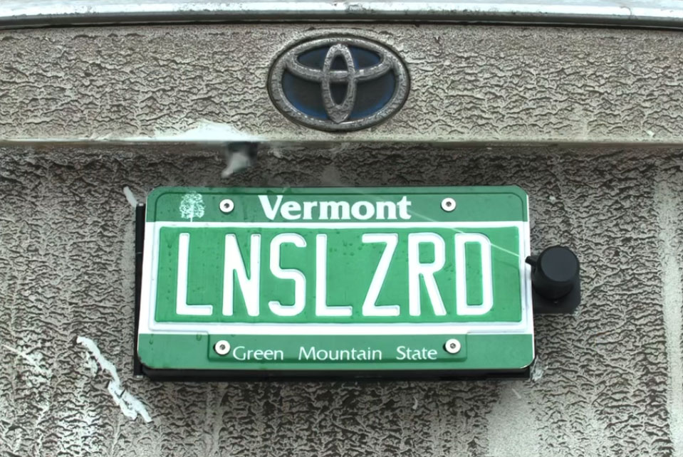 The backup camera of a Toyota with a Vermont license plate being cleaned by the Lens Lizard.