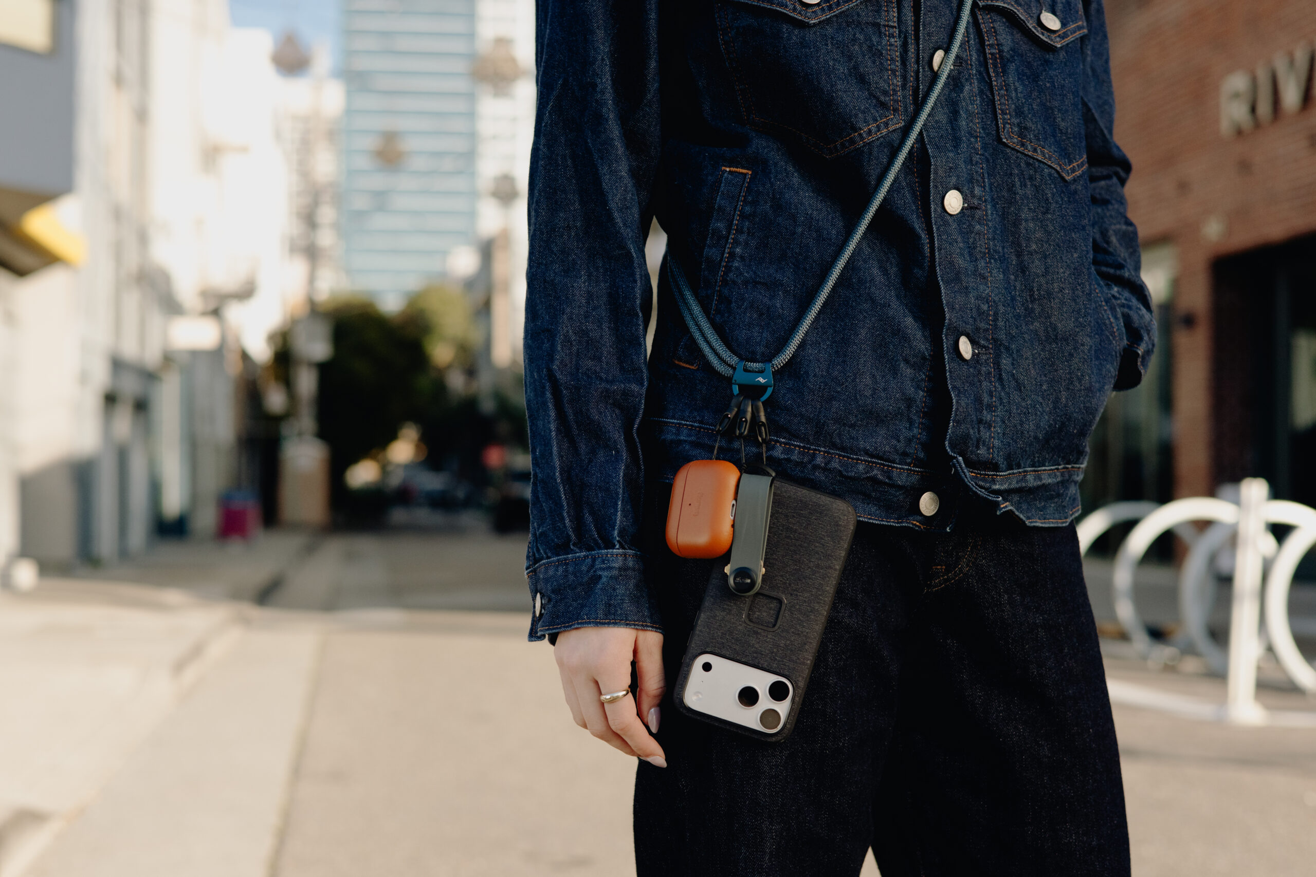 The Peak Design Crossbody Multi-Strap being used to carry a phone, earbuds, and more.