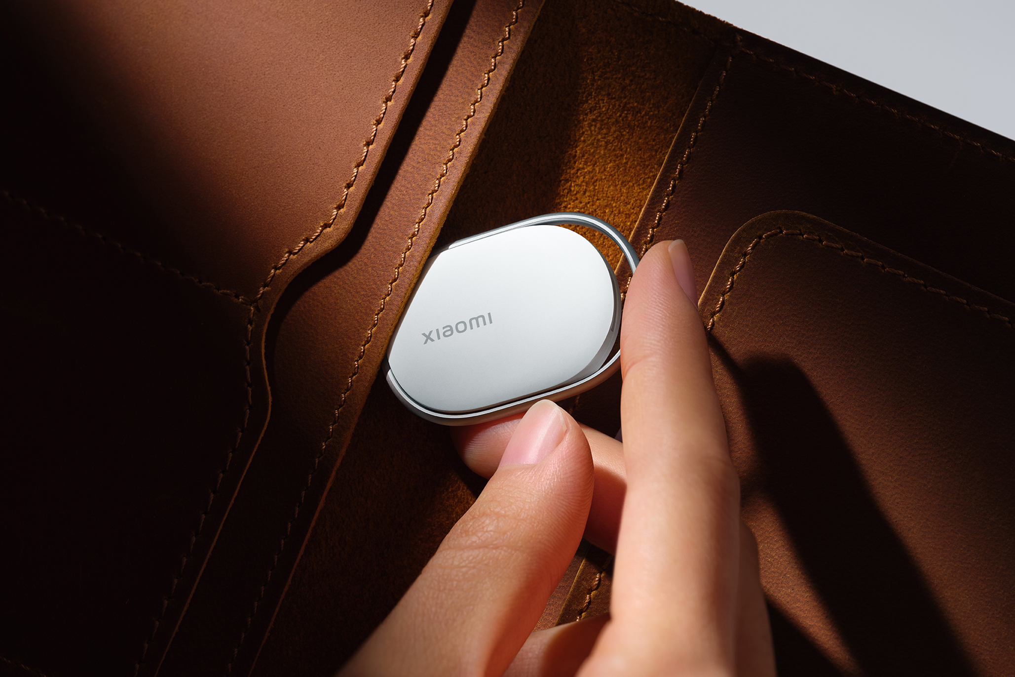 The Xiaomi Tag tracker being inserted into a brown leather wallet.
