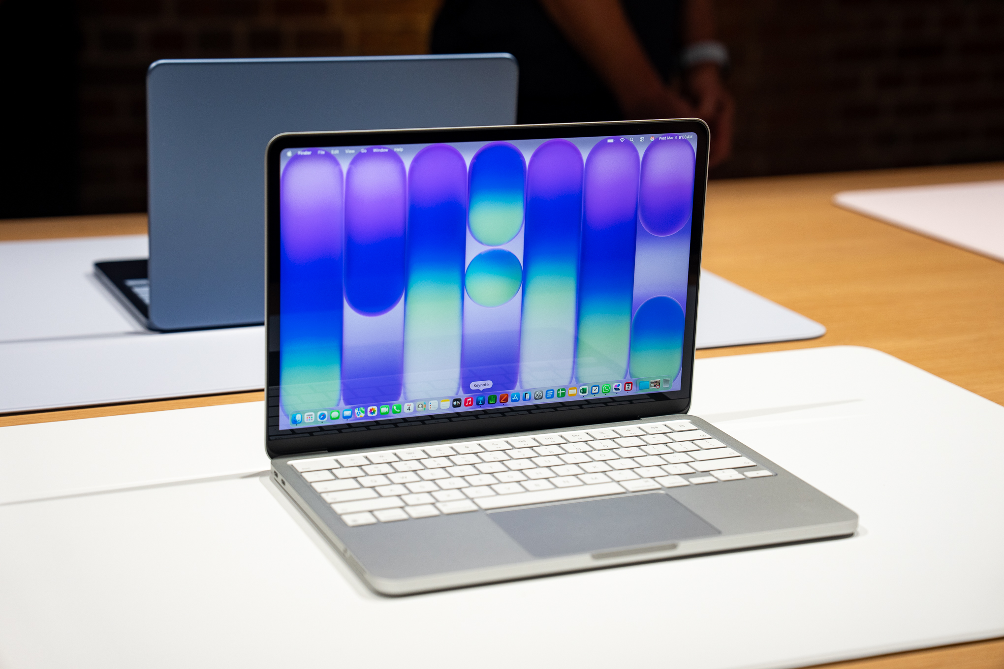A silver MacBook Neo on a desk with a blue one behind it.