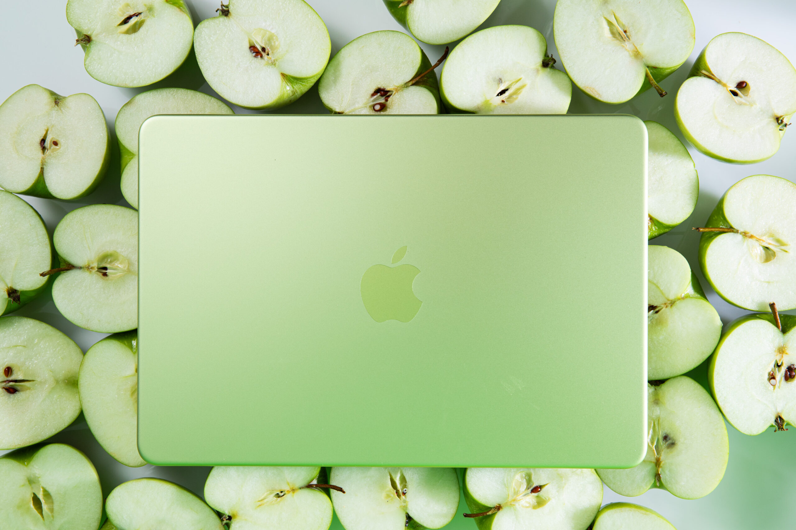 A citrus-colored MacBook Neo laptop resting on a bed of cut green apples.