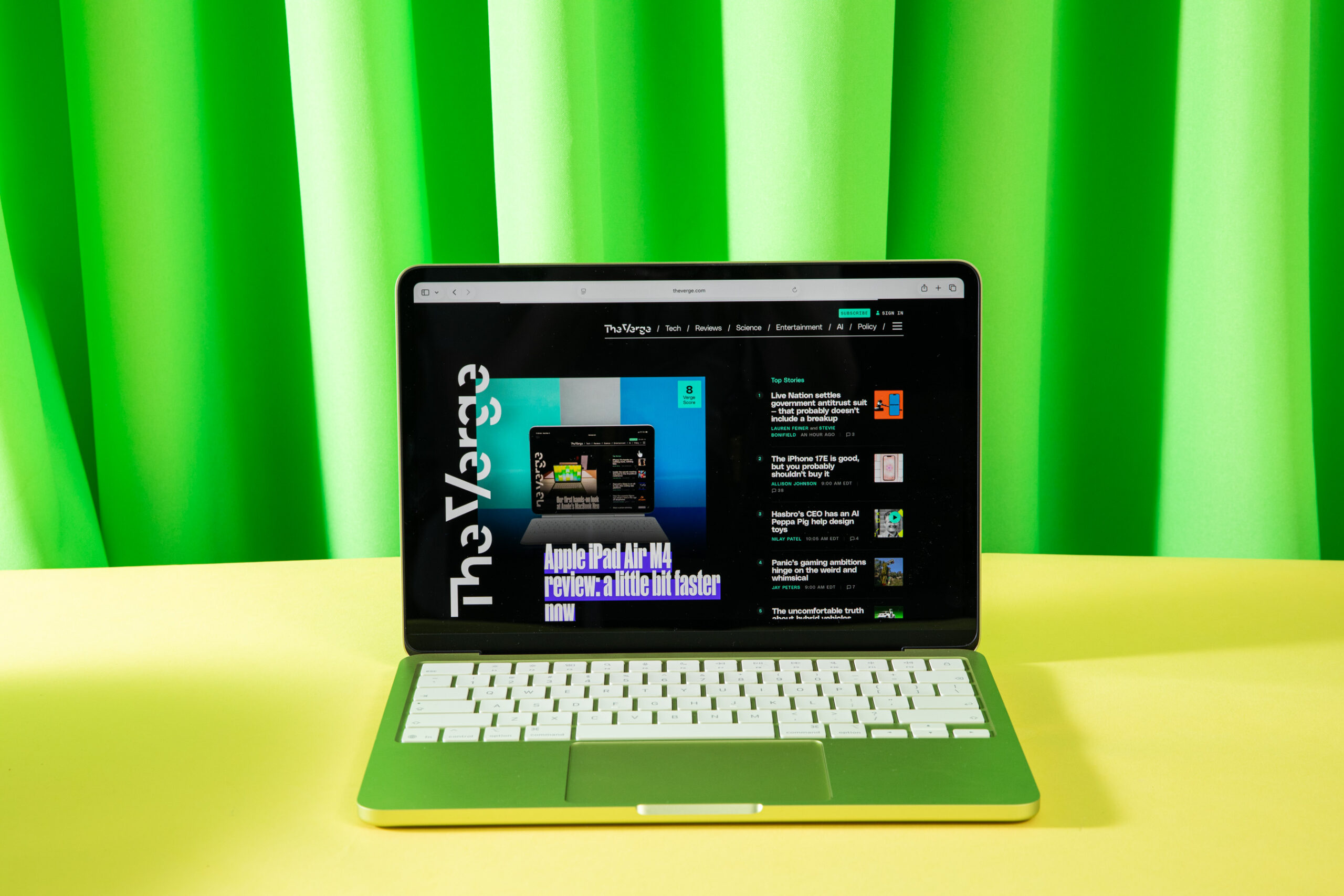 A citrust colored MacBook Neo on a yellow table in front of a green backdrop.