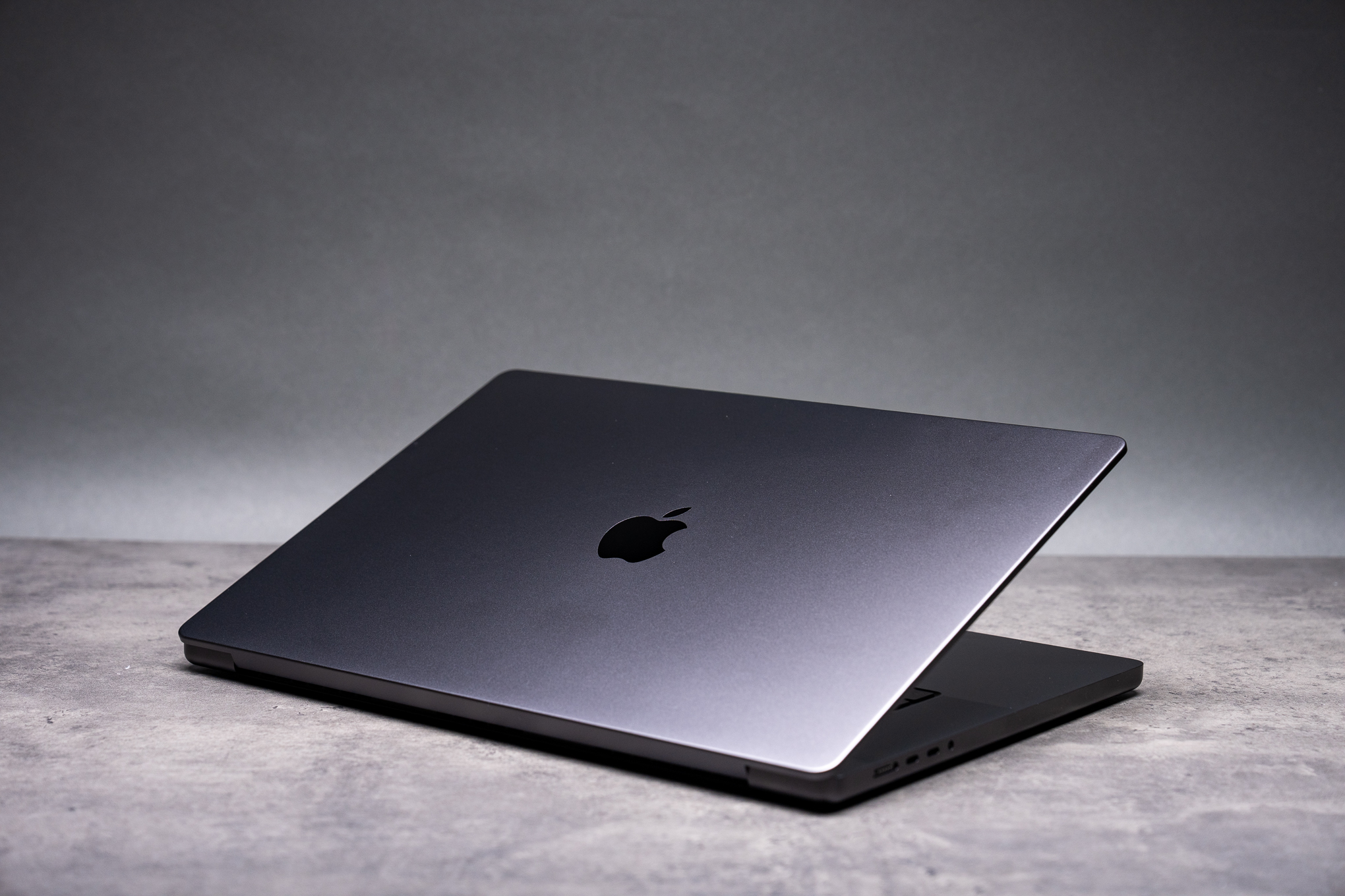 A rear view of a partially opened 16-inch MacBook Pro in space black, against a gray background.