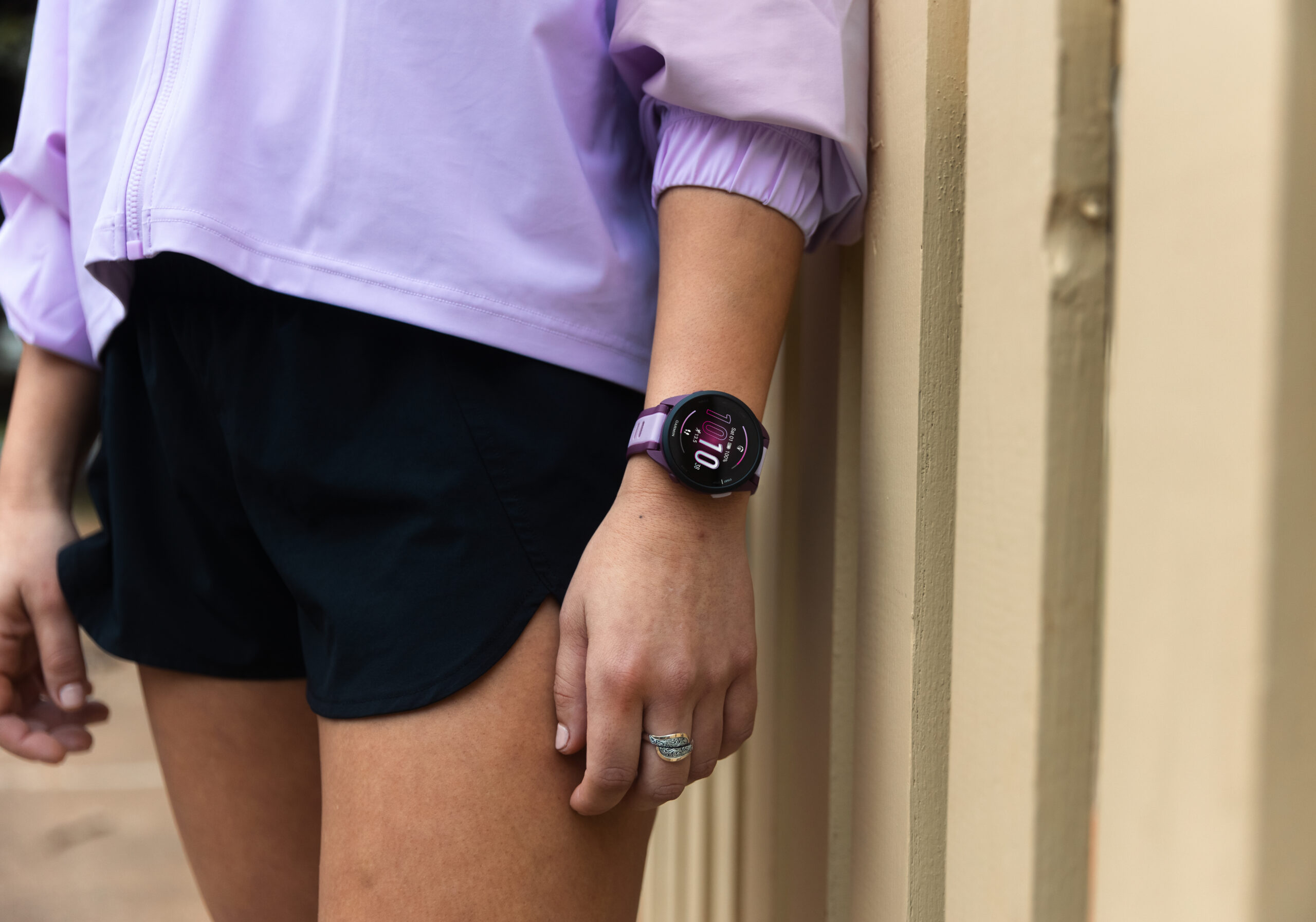Woman leaning on wall wearing purple Garmin Forerunner 165 watch