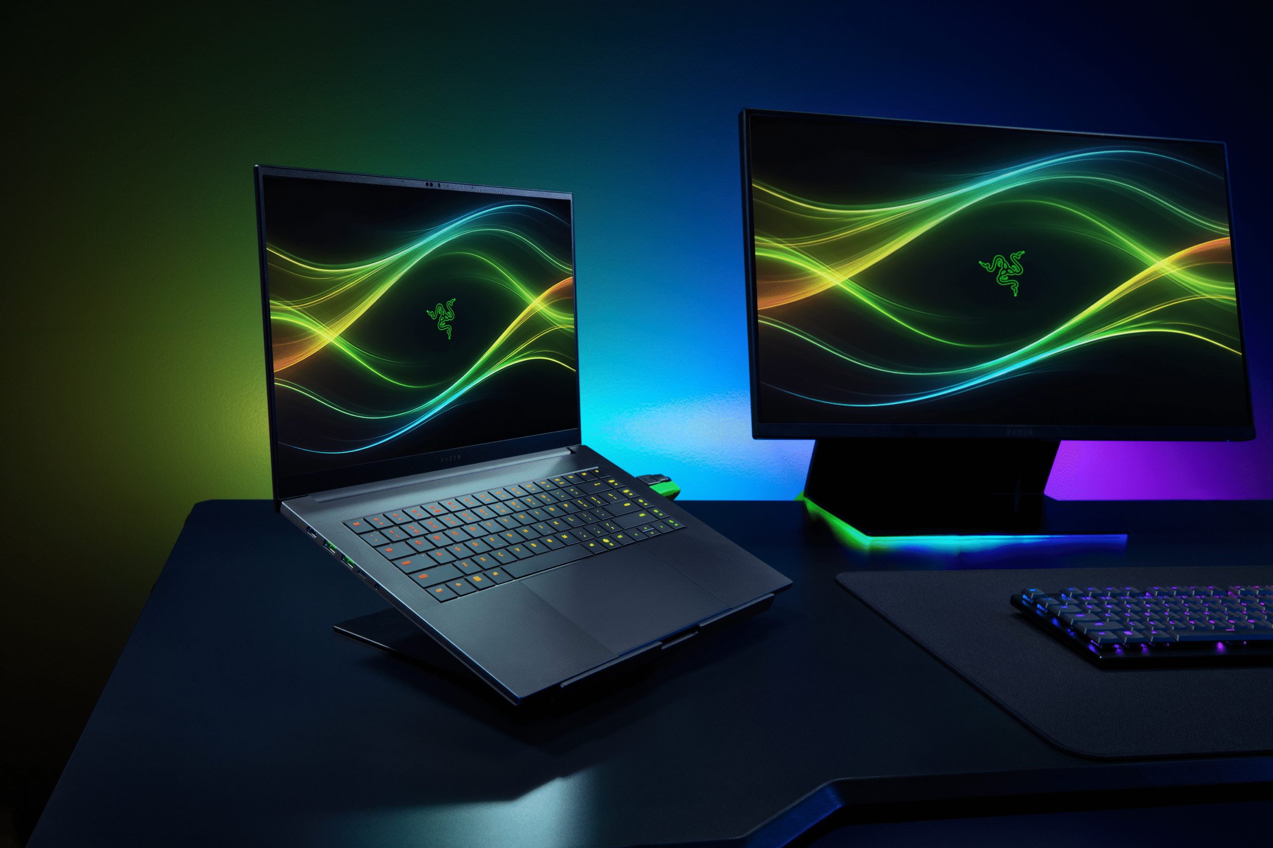A Razer Blade 16 elevated on a stand on a desk beside a monitor and keyboard.