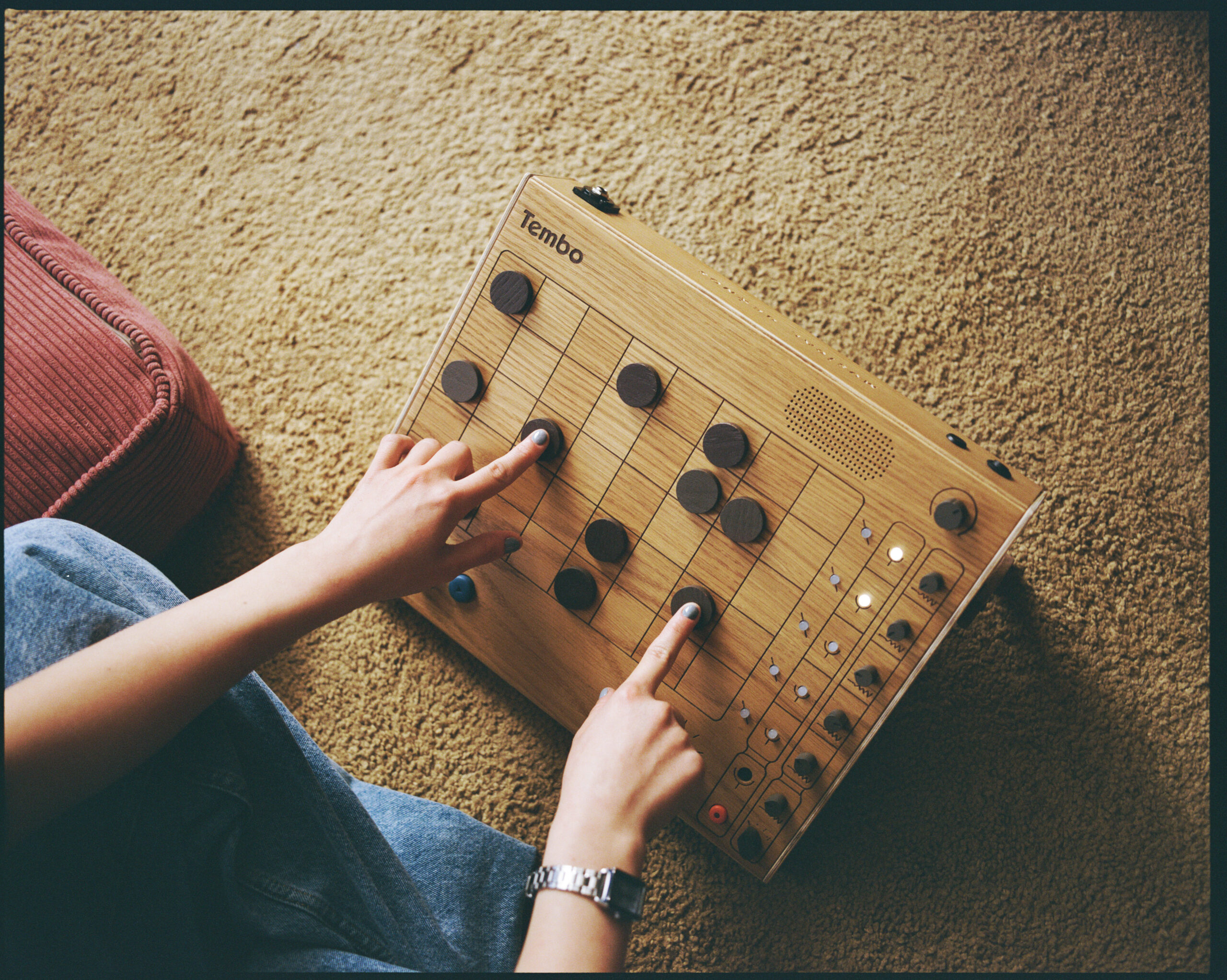 A top down view of someone playing Tembo, a drum machine made out of wood that looks very much like a checkerboard.