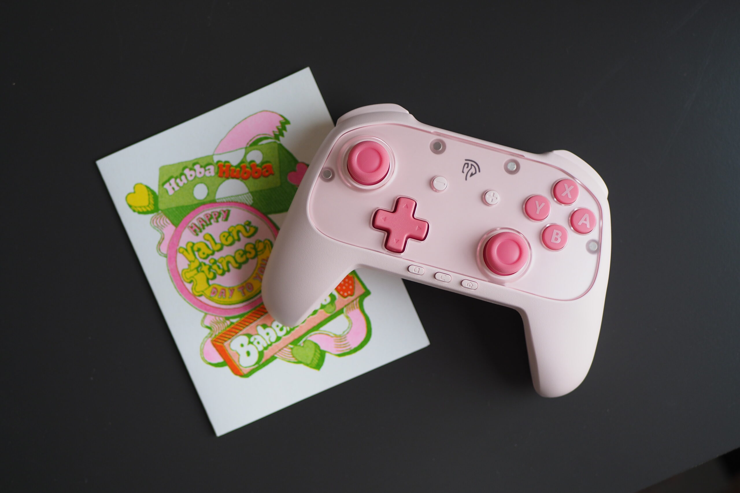 An image of the pink EasySMX S10 Lite next to a Valentine’s Day themed card with similar colors.