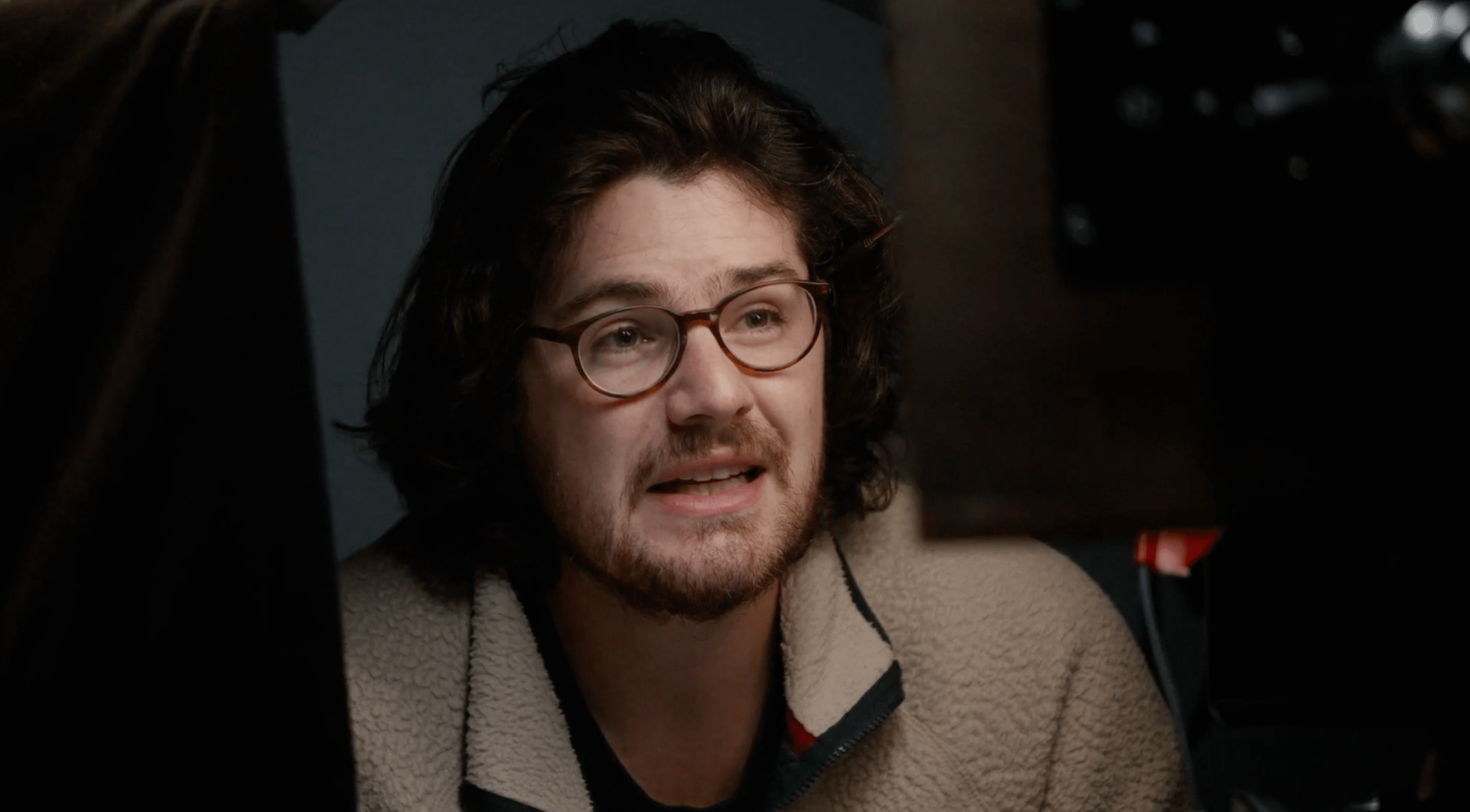 A bearded man wearing glasses making a face of discomfort at someone off-camera.