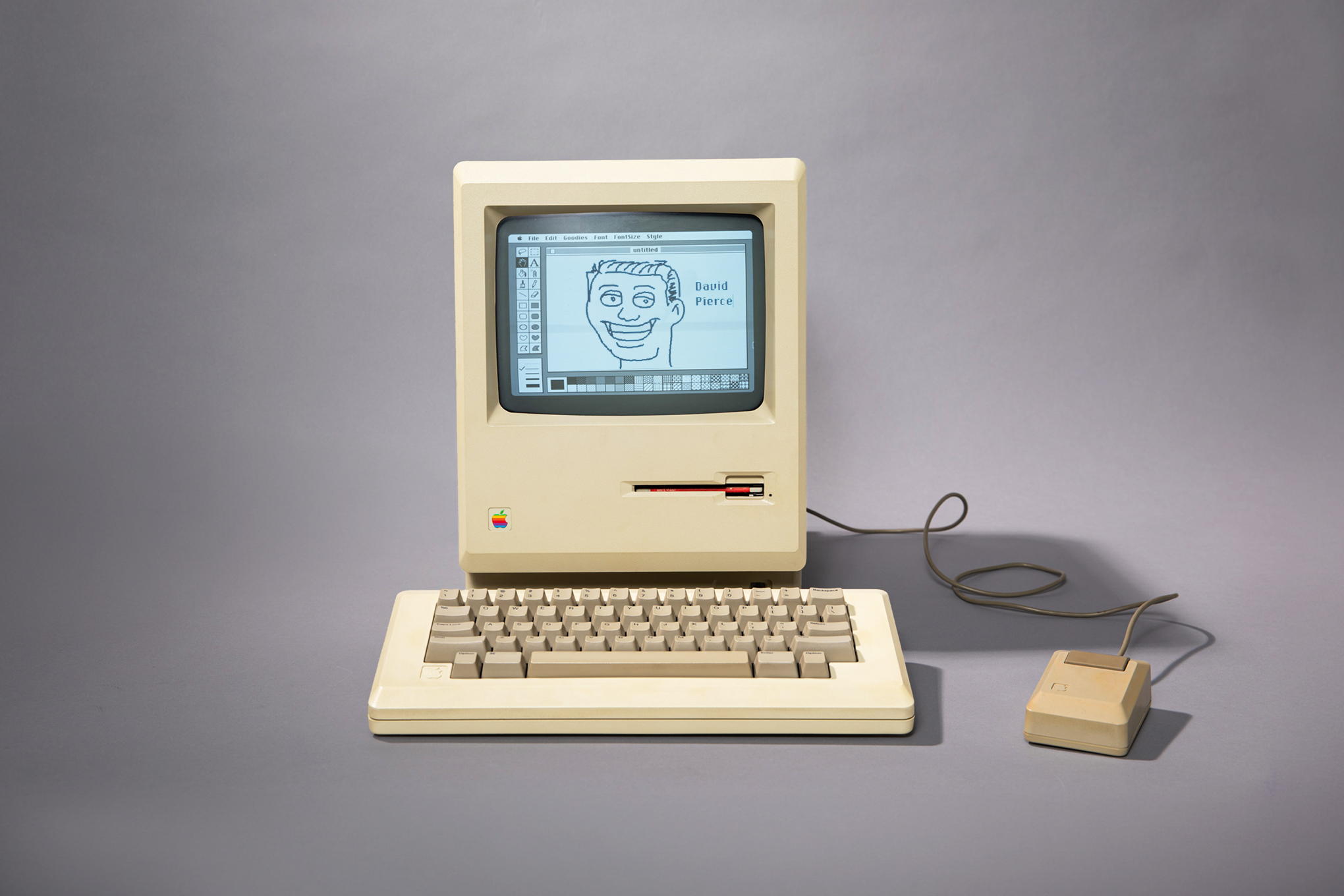 A photo of a 1984 Macintosh on a gray background.