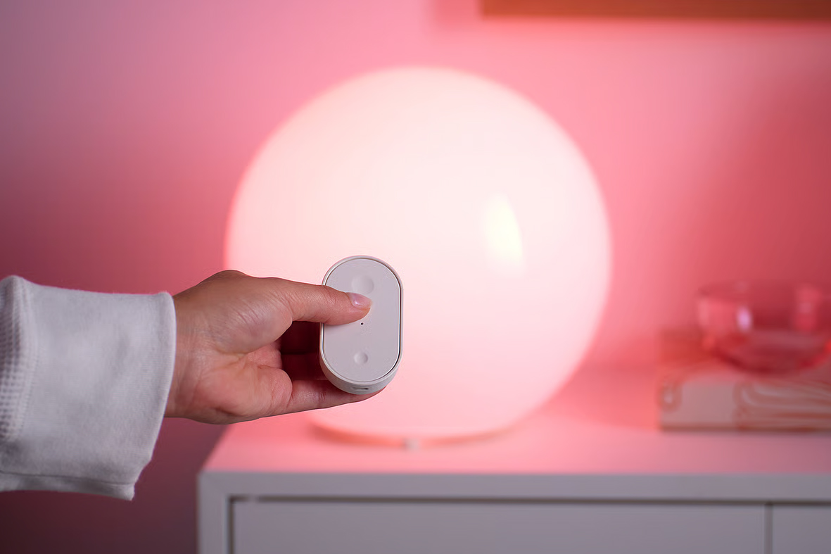 A person uses a small remote to control a lamp featuring an Ikea smart bulb.
