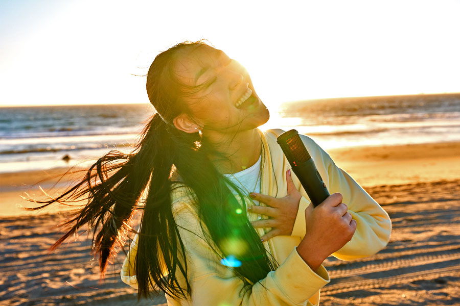 A person on a beach sings into one of JBL’s wireless EasySing microphones.