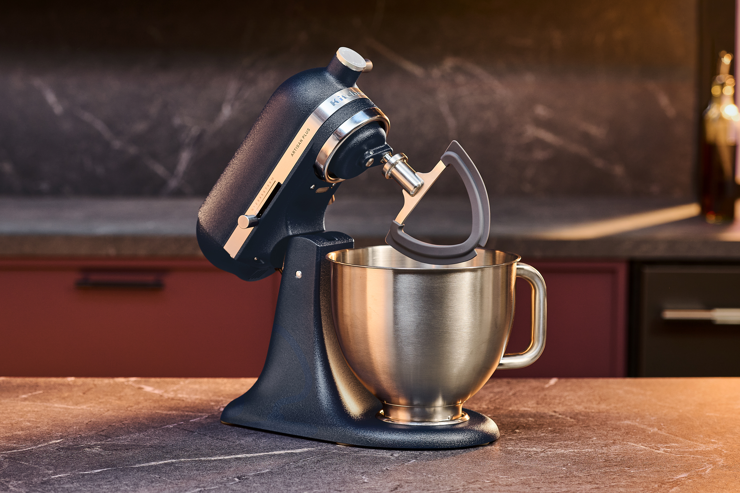 A KitchenAid Artisan Plus Stand Mixer sitting on a kitchen island with a beater attached and raised.