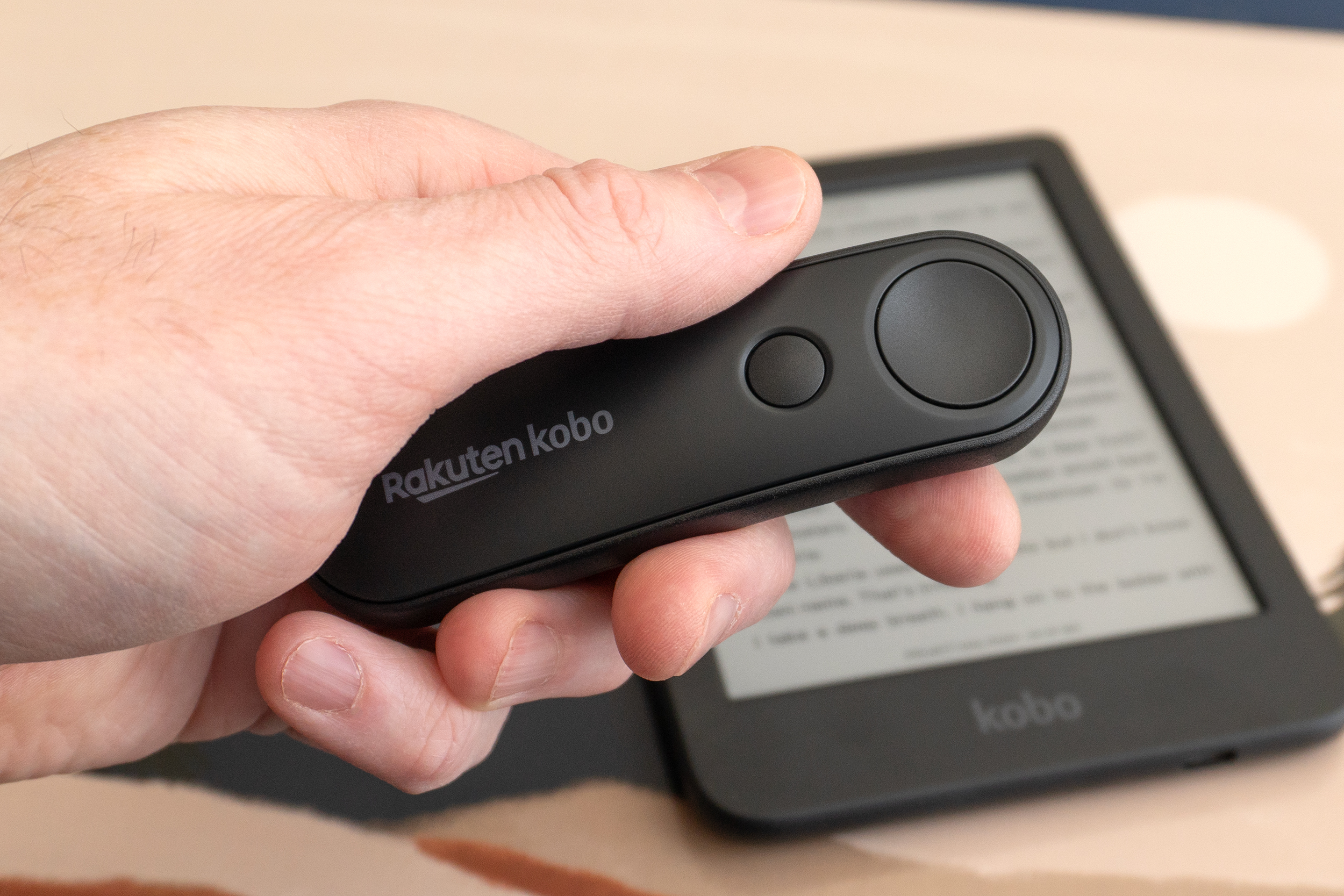 A hand holds the Kobo Remote over a Kobo e-reader.