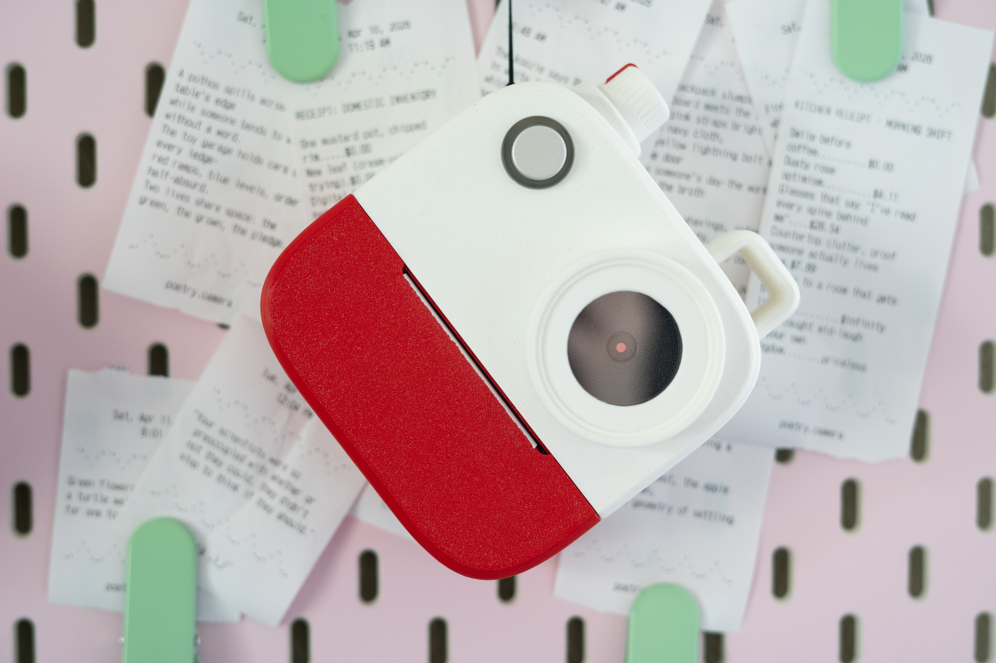 Poetry Camera shown in front of a pegboard with printed poem receipts behind it