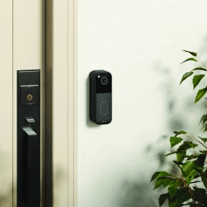 A black video doorbell camera on a white exterior wall next to a front door.