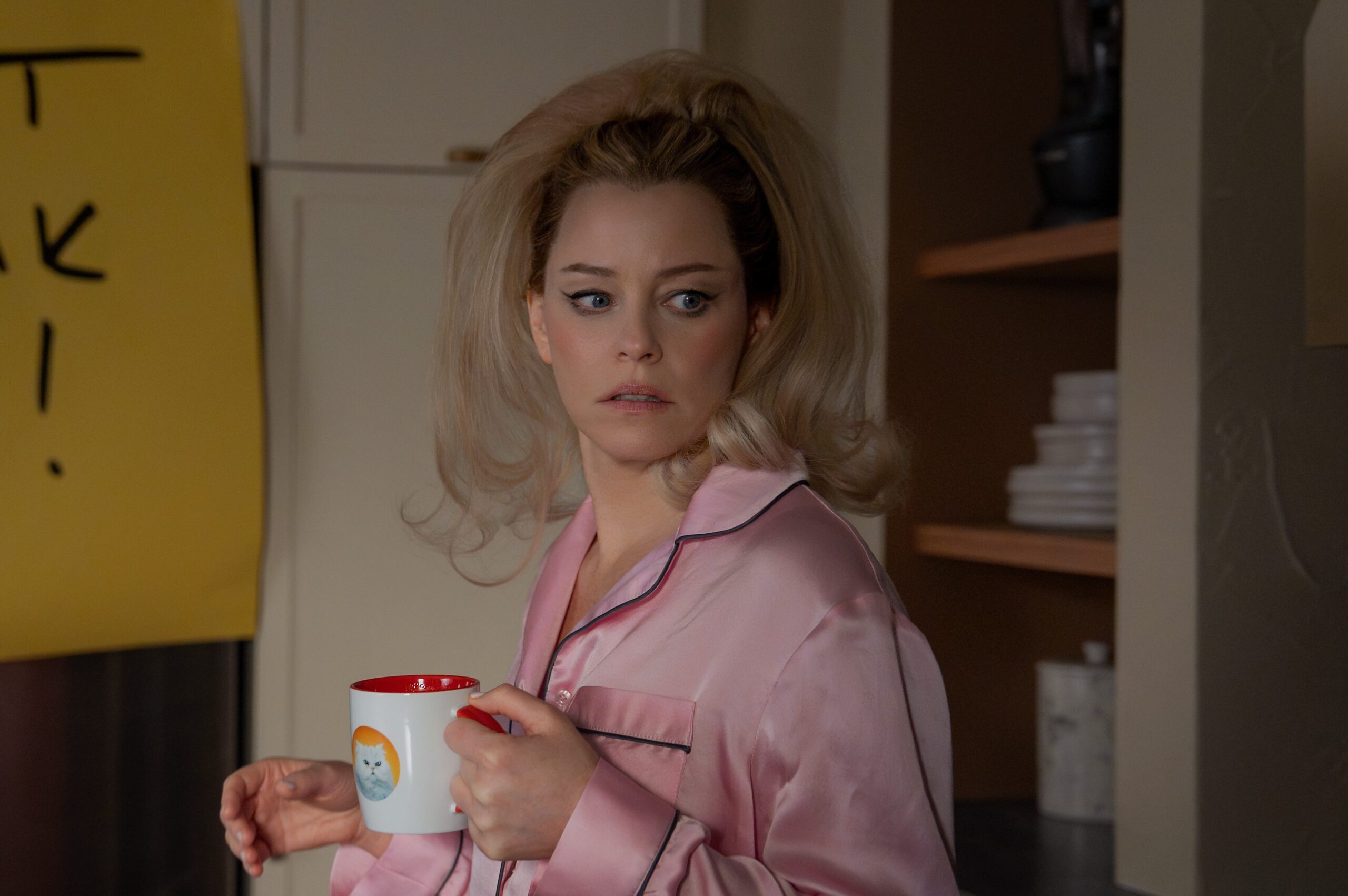 A woman in pink pajamas standing in a kitchen were a massive post-it with the sentence “don’t freak out” is pasted to the front of a refrigerator.