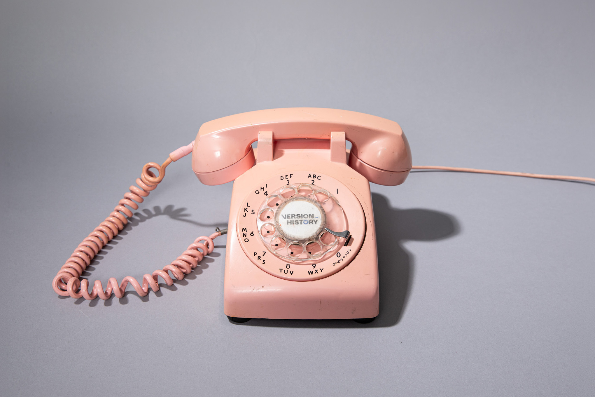 A photo of a pink landline phone on a gray background.