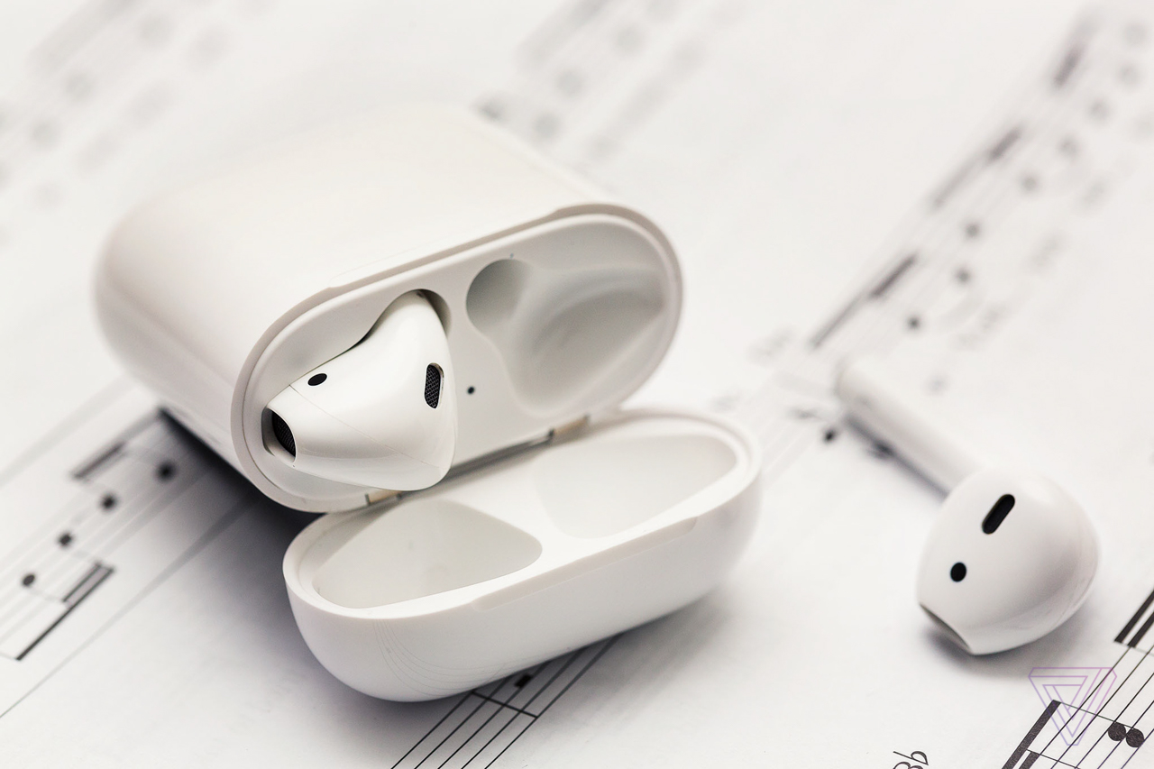 The original AirPods, one in their open case and one next to the case, on a sheet of music.