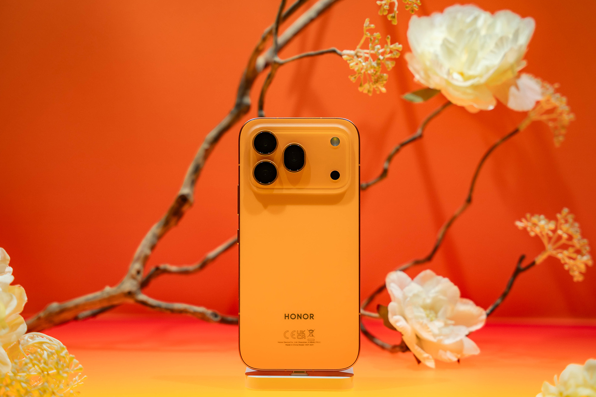 Honor 600 Pro in orange, in front of an orange backdrop with flowers