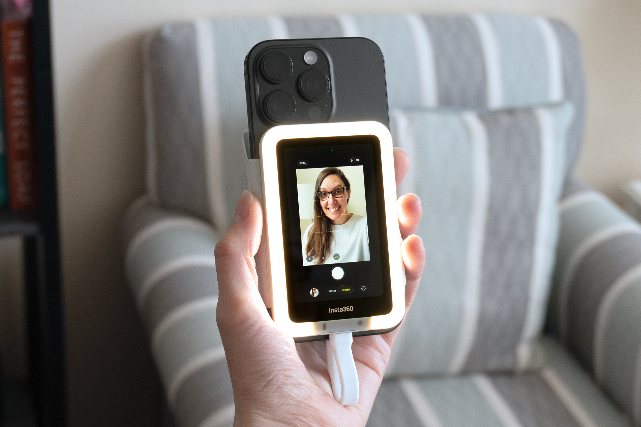 A person holds a smartphone at arm’s length to take a selfie using Insta360’s Snap screen accessory attached.