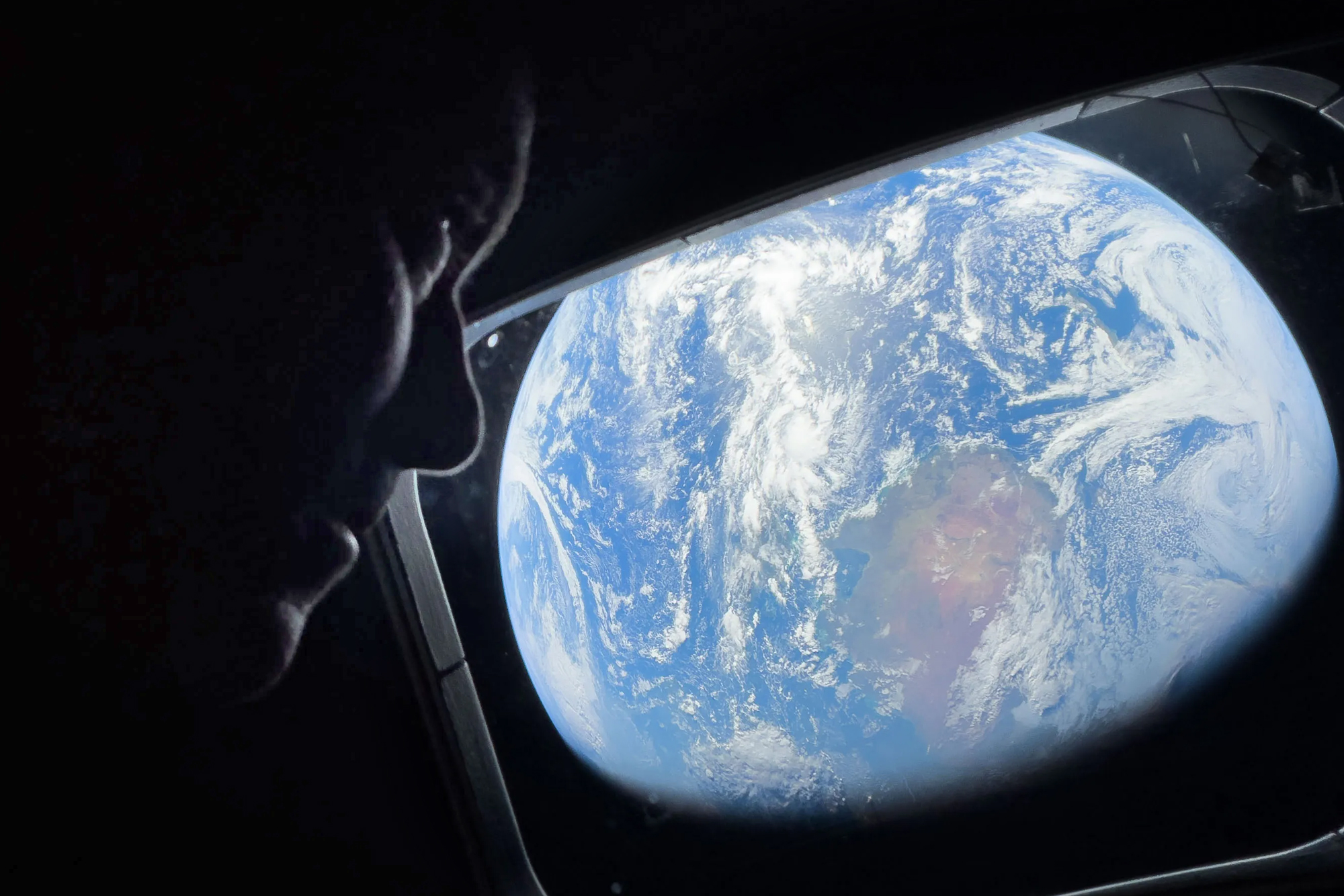Astronaut and Artemis II Commander Reid Wiseman peers out of one of the Orion spacecraft’s main cabin windows, looking back at Earth, as the crew travels towards the Moon.