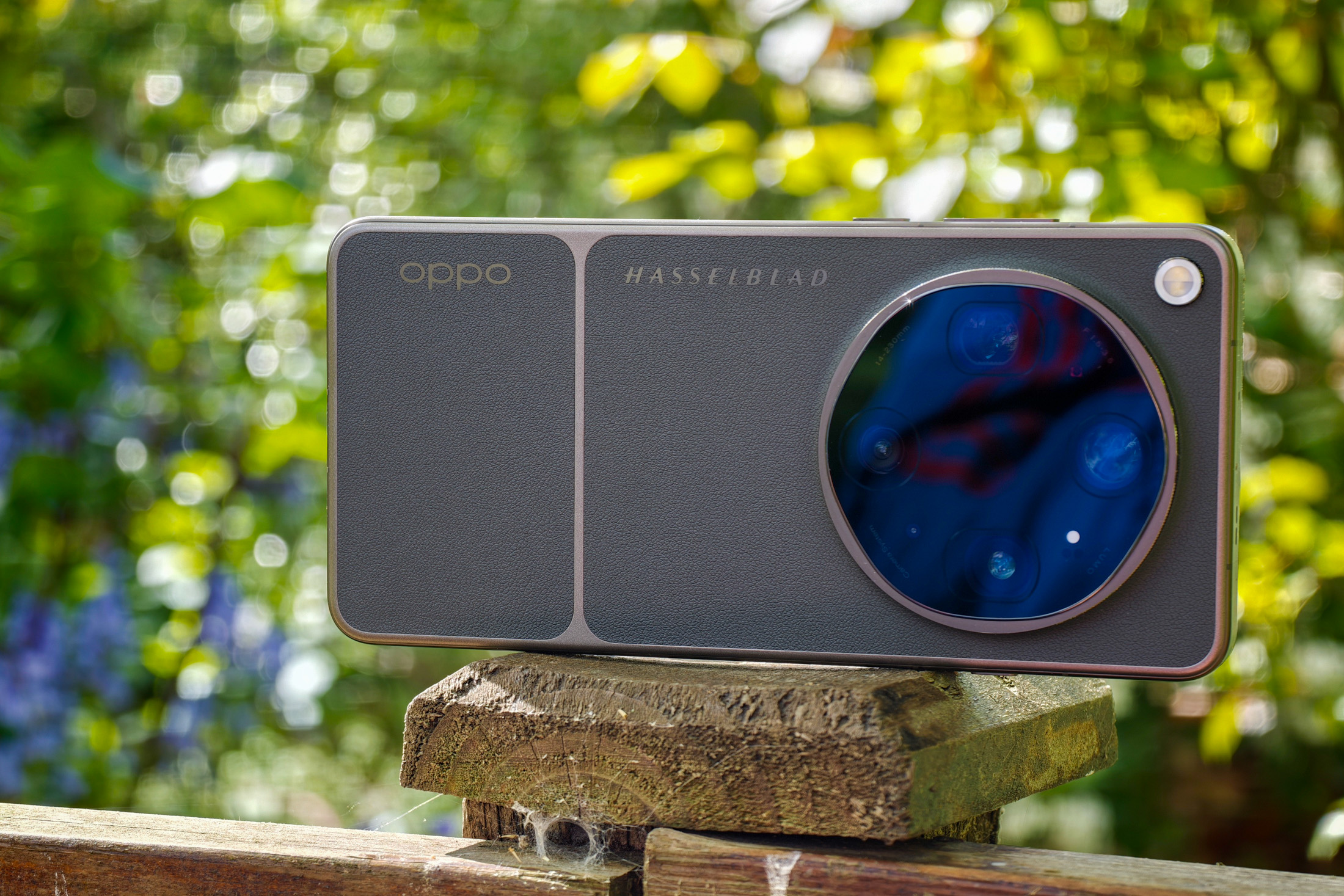 Photo of Oppo Find X9 Ultra resting horizontally on a wooden post in front of green plants