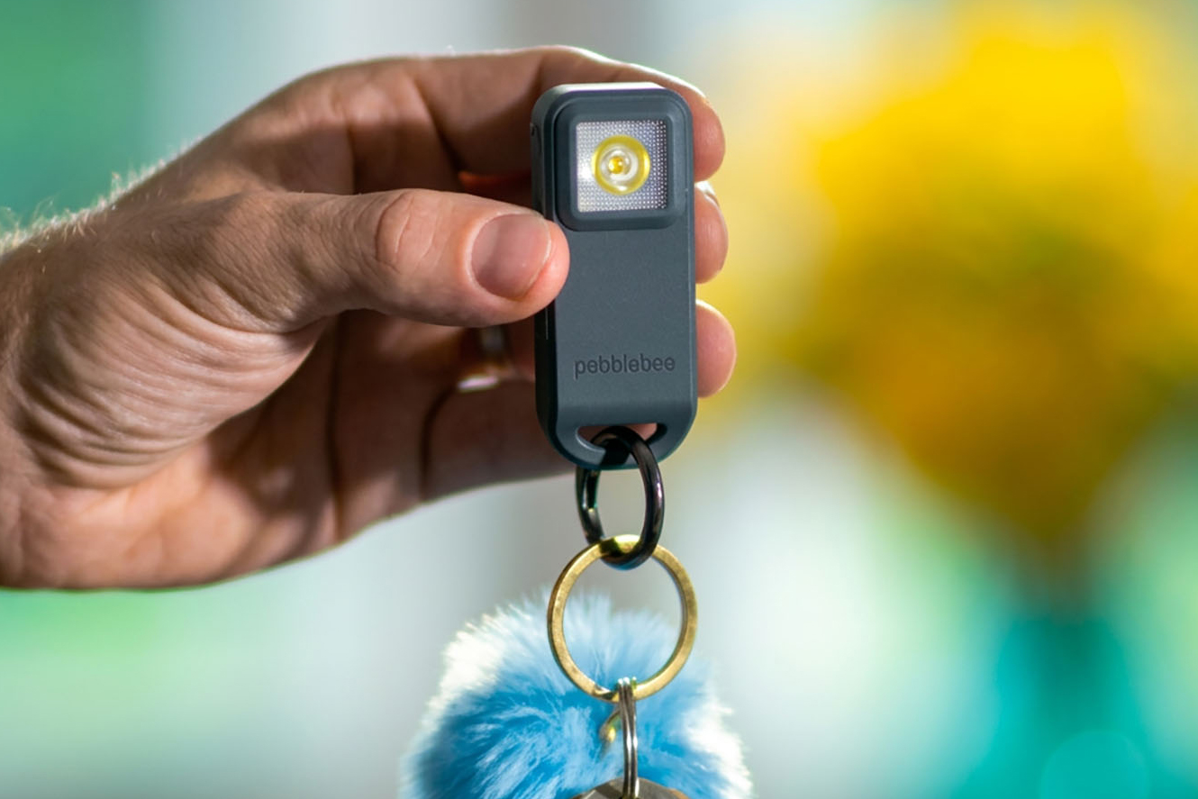 A person holds the Pebblebee Halo personal safety device attached to their keys.