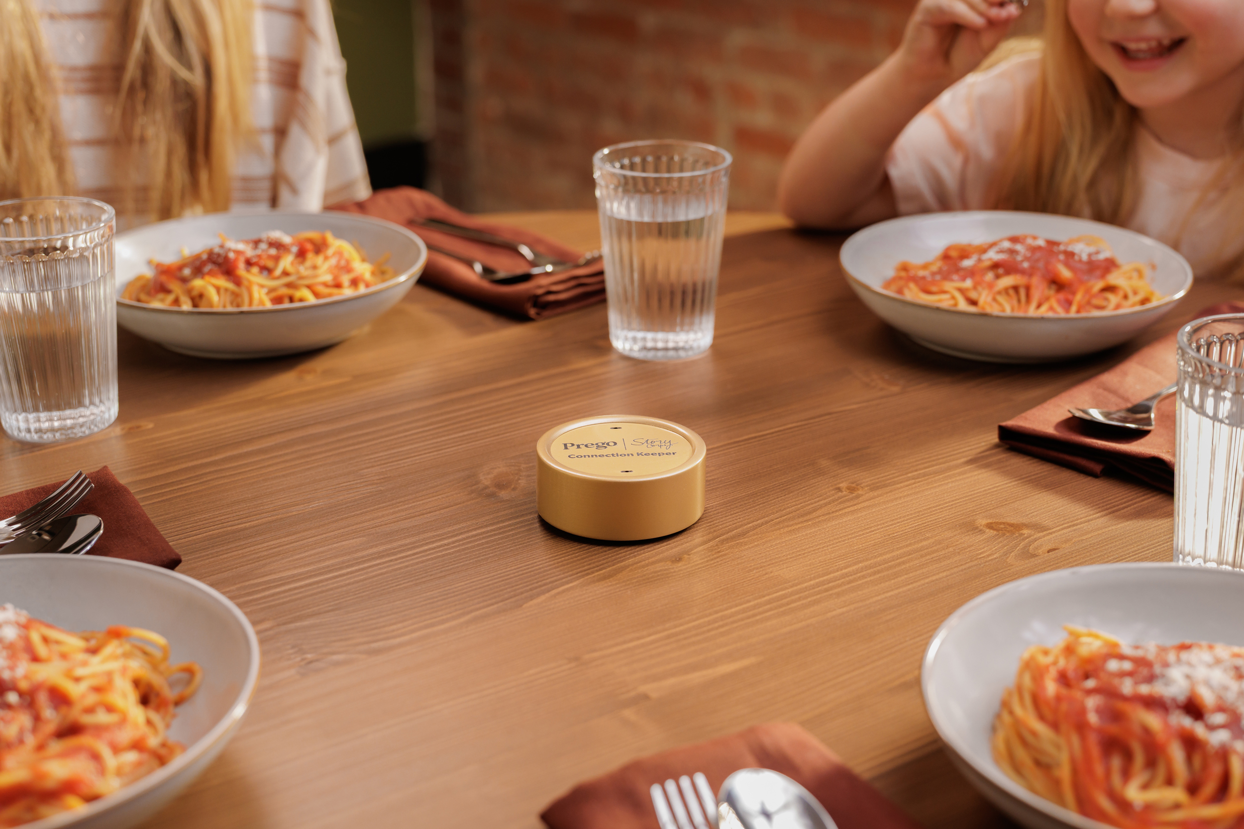 A family sits around a dinner table with plates of spaghetti and Prego’s Connection Keeper device in the middle.
