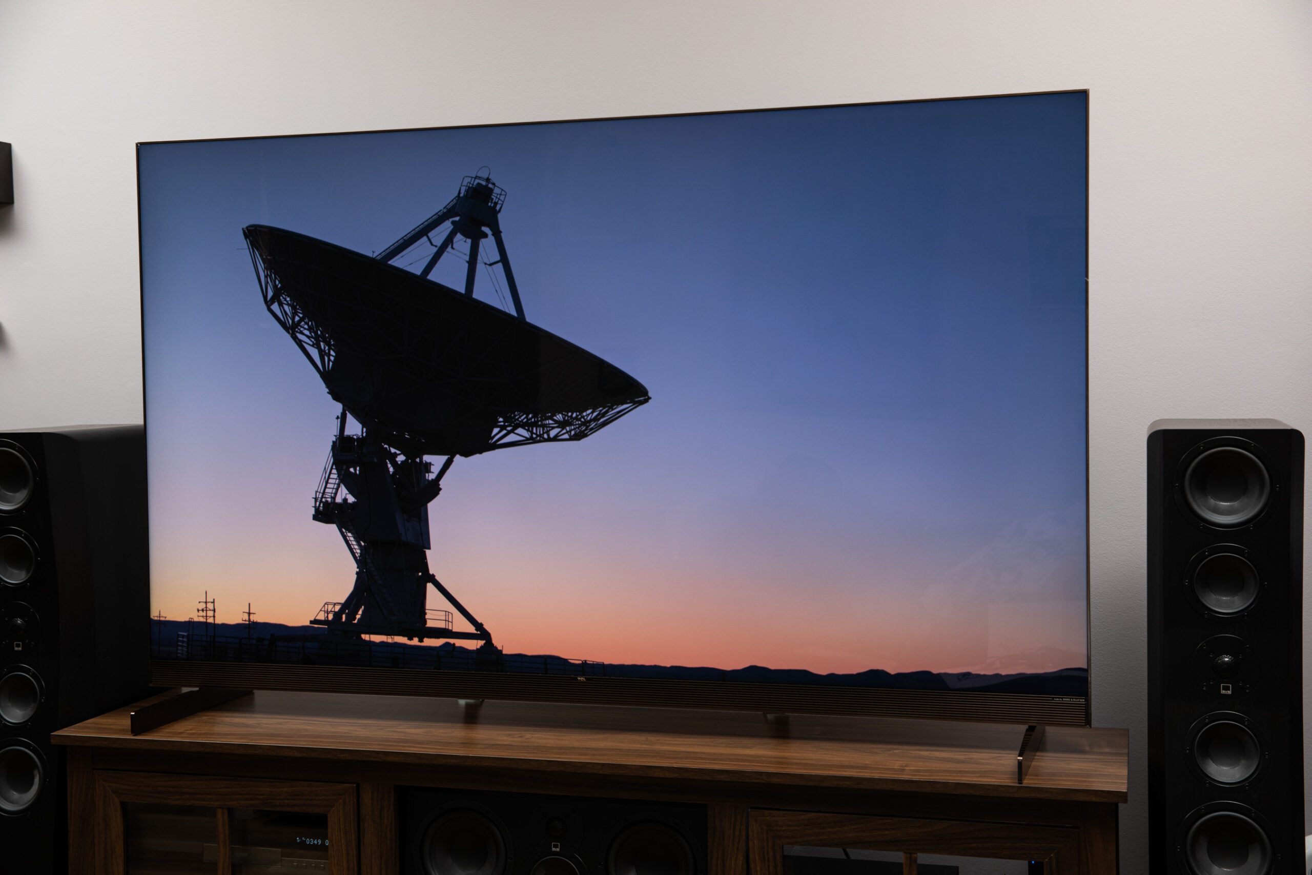 The TCL X11L TV on a dark wood stand with the image of a radio telescope.