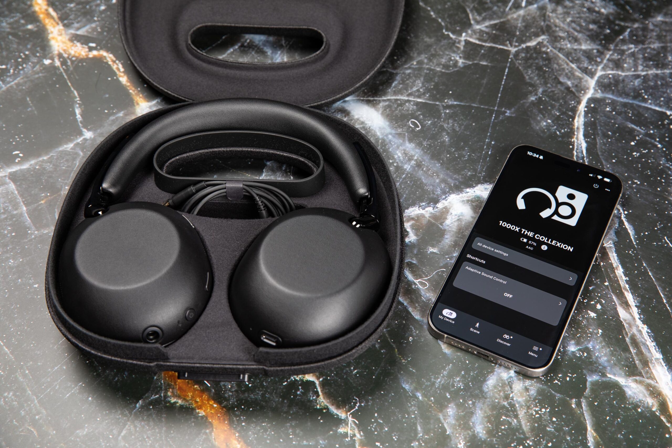 The Sony 1000X The Collexion headphones in their open case next to an iPhone on a marble surface.