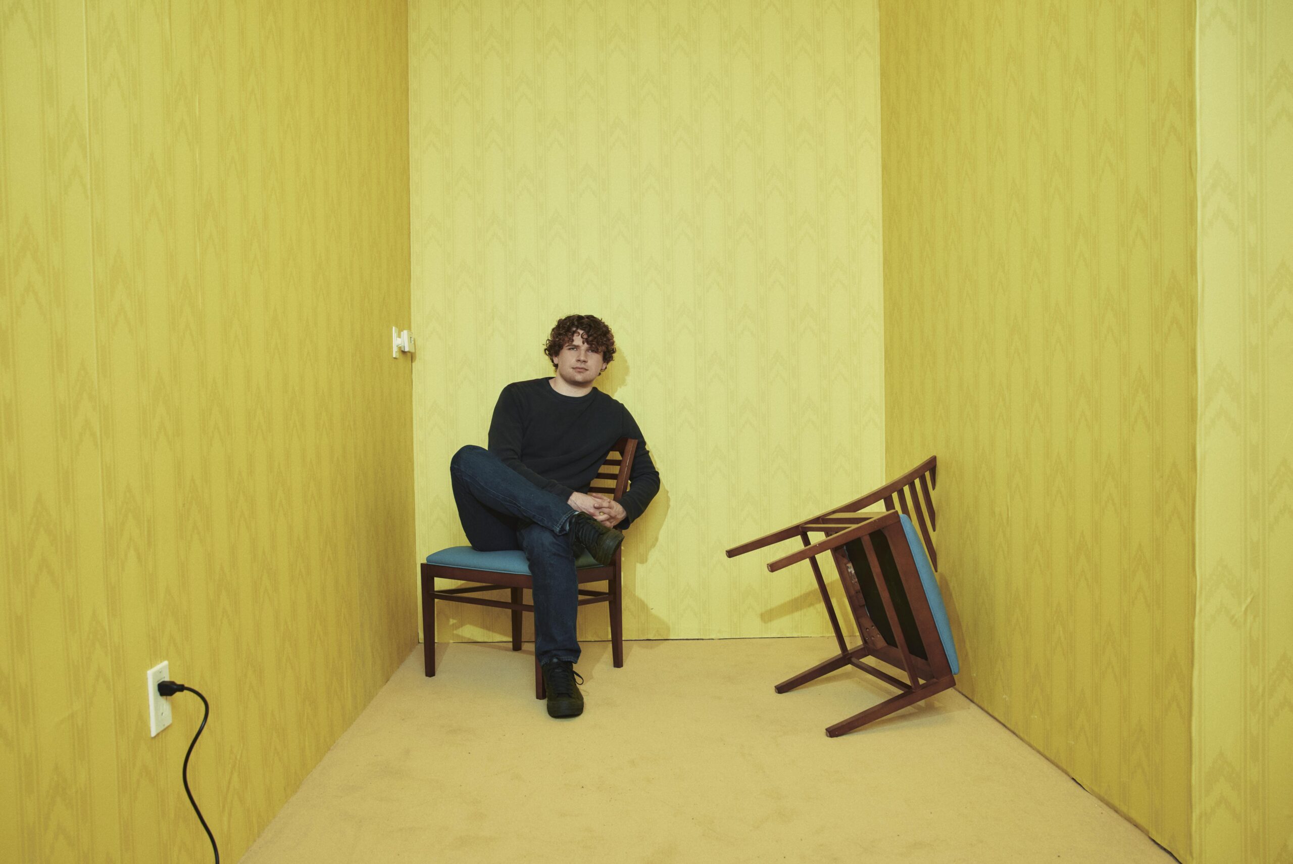 Director Kane Parsons sitting in a chair  in a small room where another chair seems to be clipping into a wall.