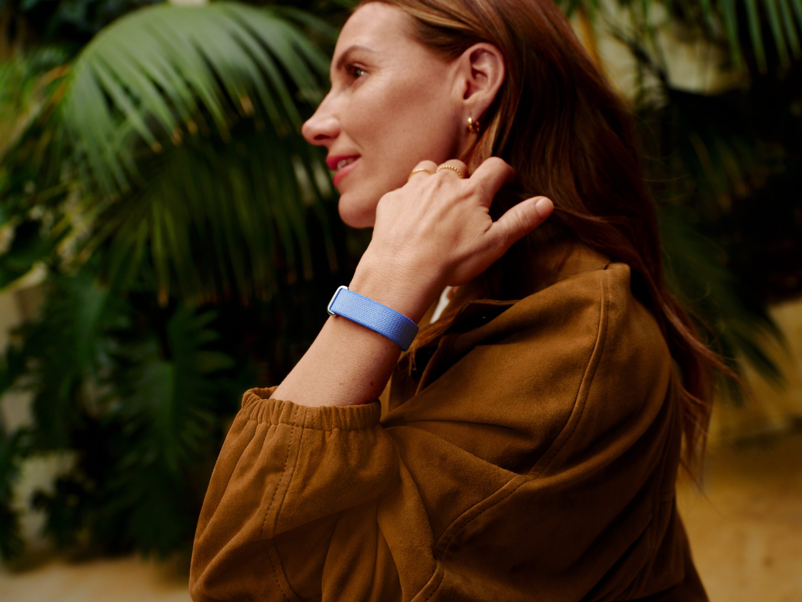 Woman wearing the lavender Fitbit Air on her wrist while reaching her hand up to her ear to brush away hair. 