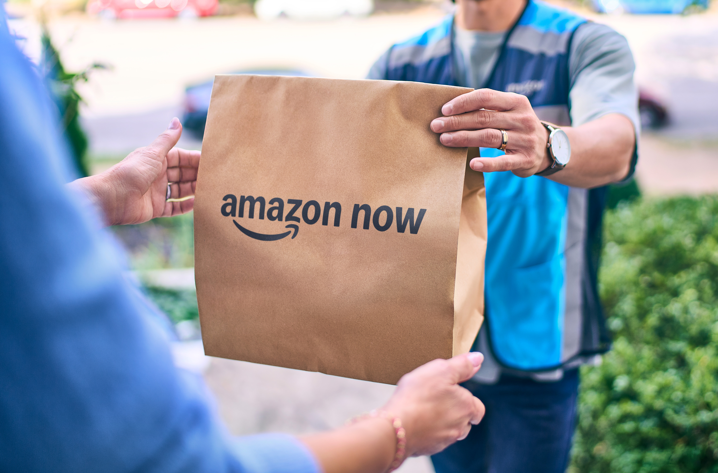 A delivery person hands over a paper bag labelled with Amazon Now.
