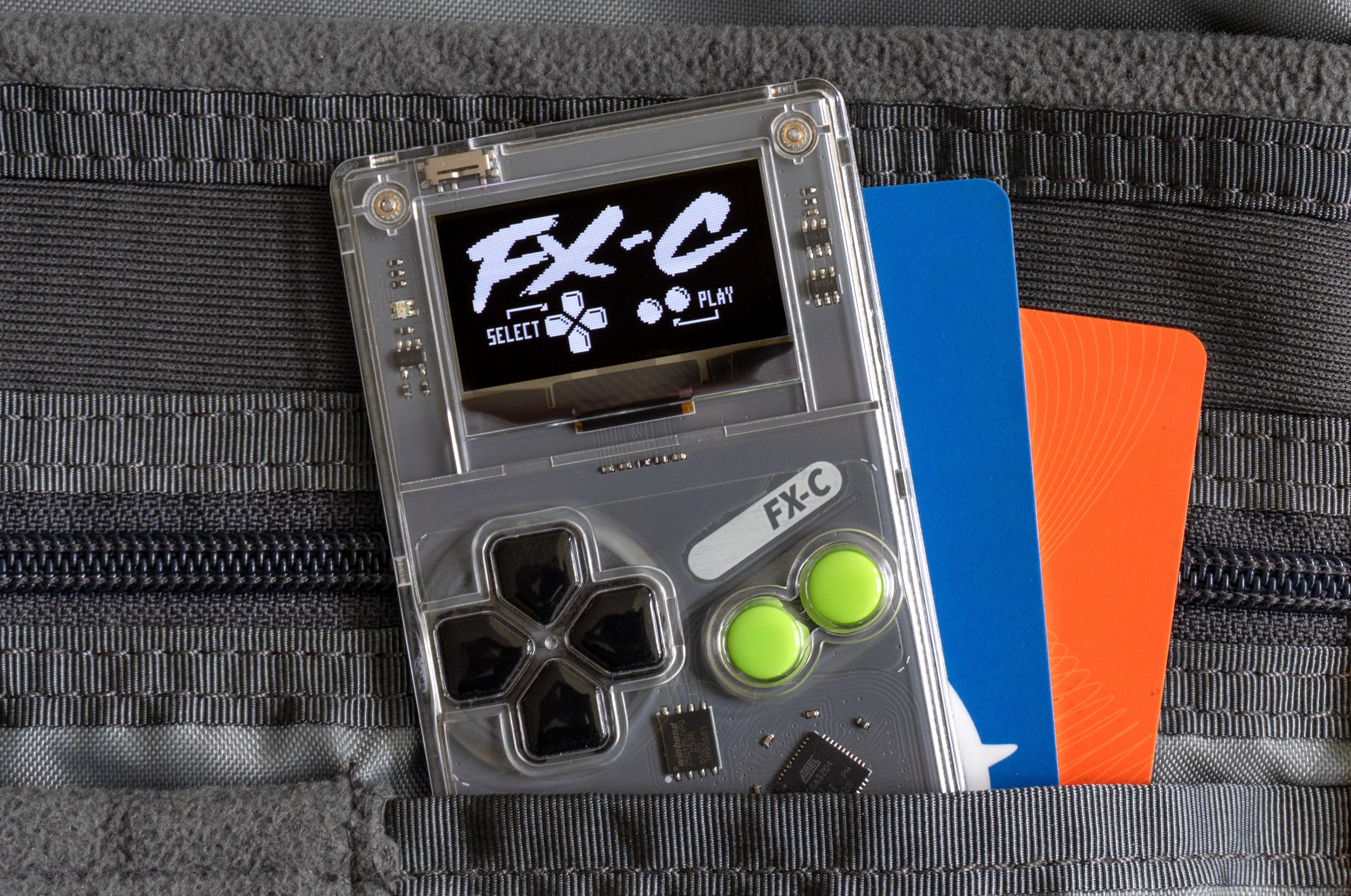 The Arduboy FX-C sticking out of a pocket inside a backpack alongside a couple of other cards.
