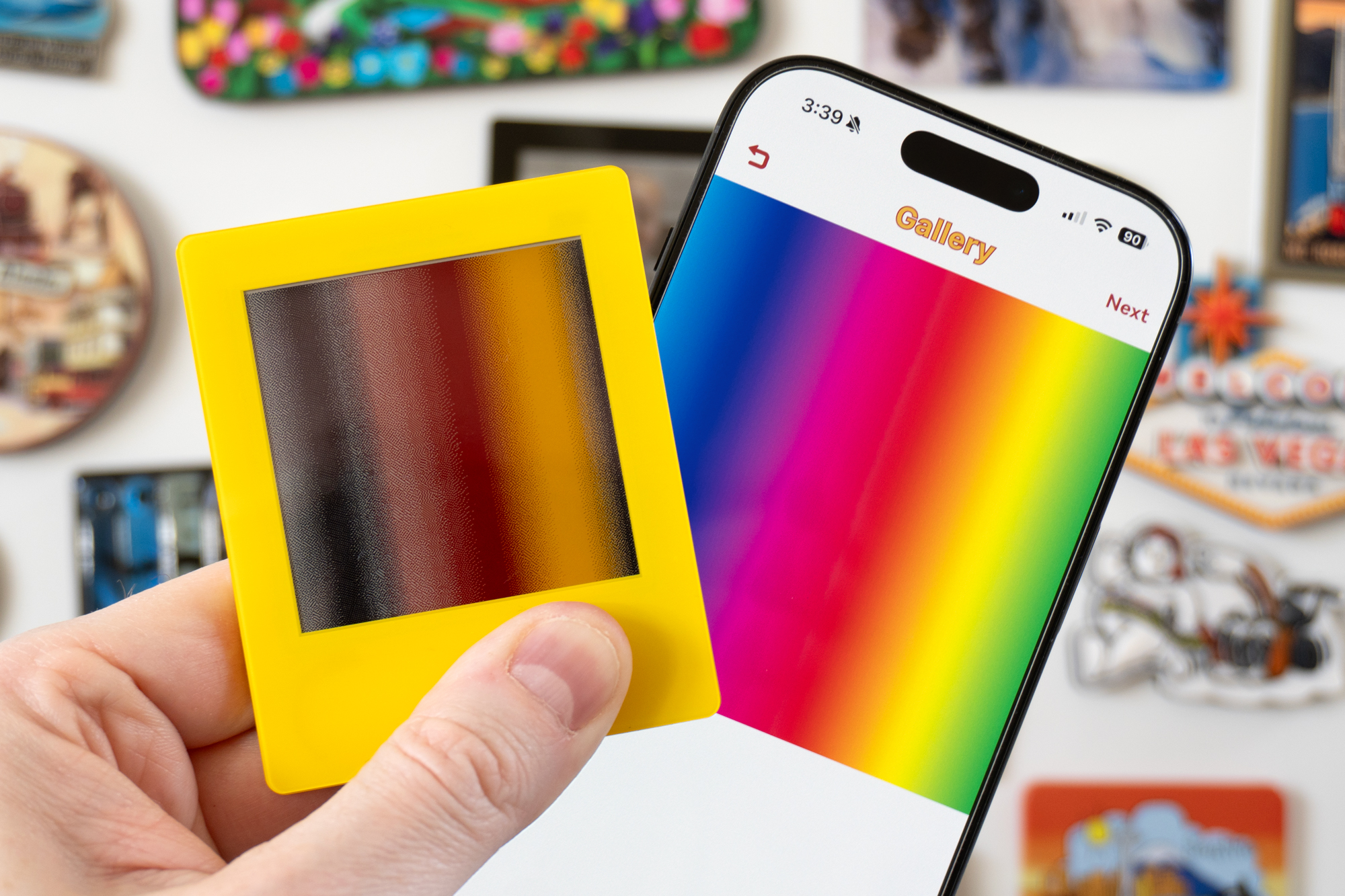 A person holds the VidaBay Snap photo frame next to an iPhone while both display a rainbow gradient image.