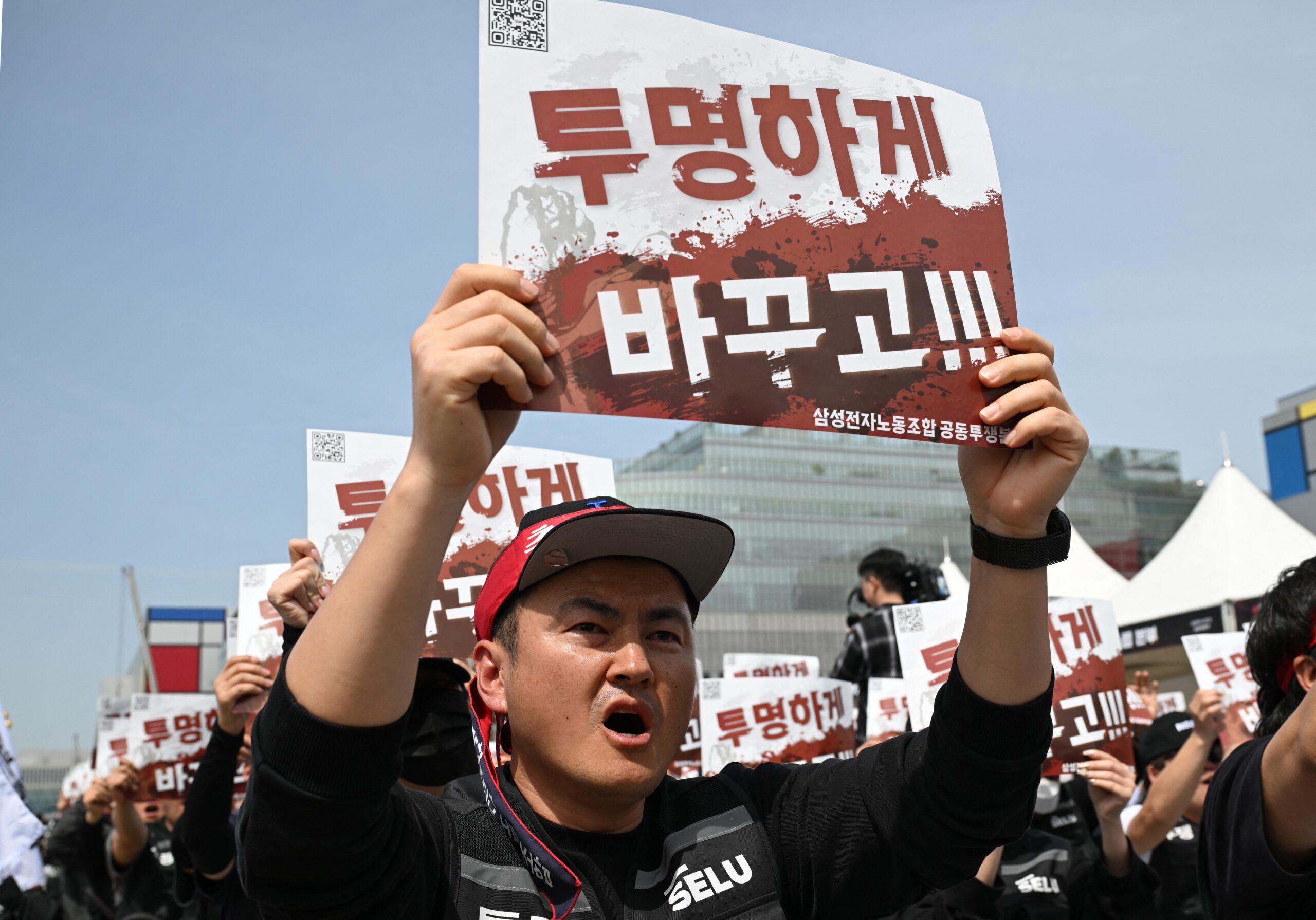 Members of the Samsung Electronics labour union hold signs reading "Change it to be transparent!" as they stage a mass rally demanding the removal of a cap on performance bonuses, outside the company's foundry and semiconductor factory in Pyeongtaek on April 23, 2026