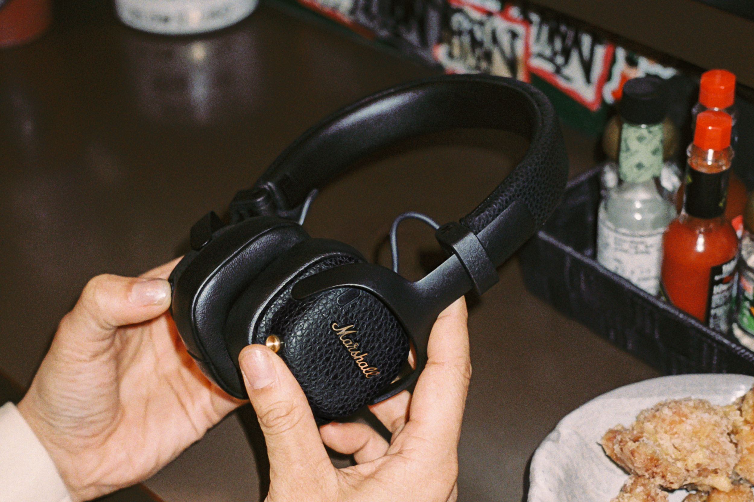A person holds the Marshall Milton A.N.C. wireless headphones over a dining counter.