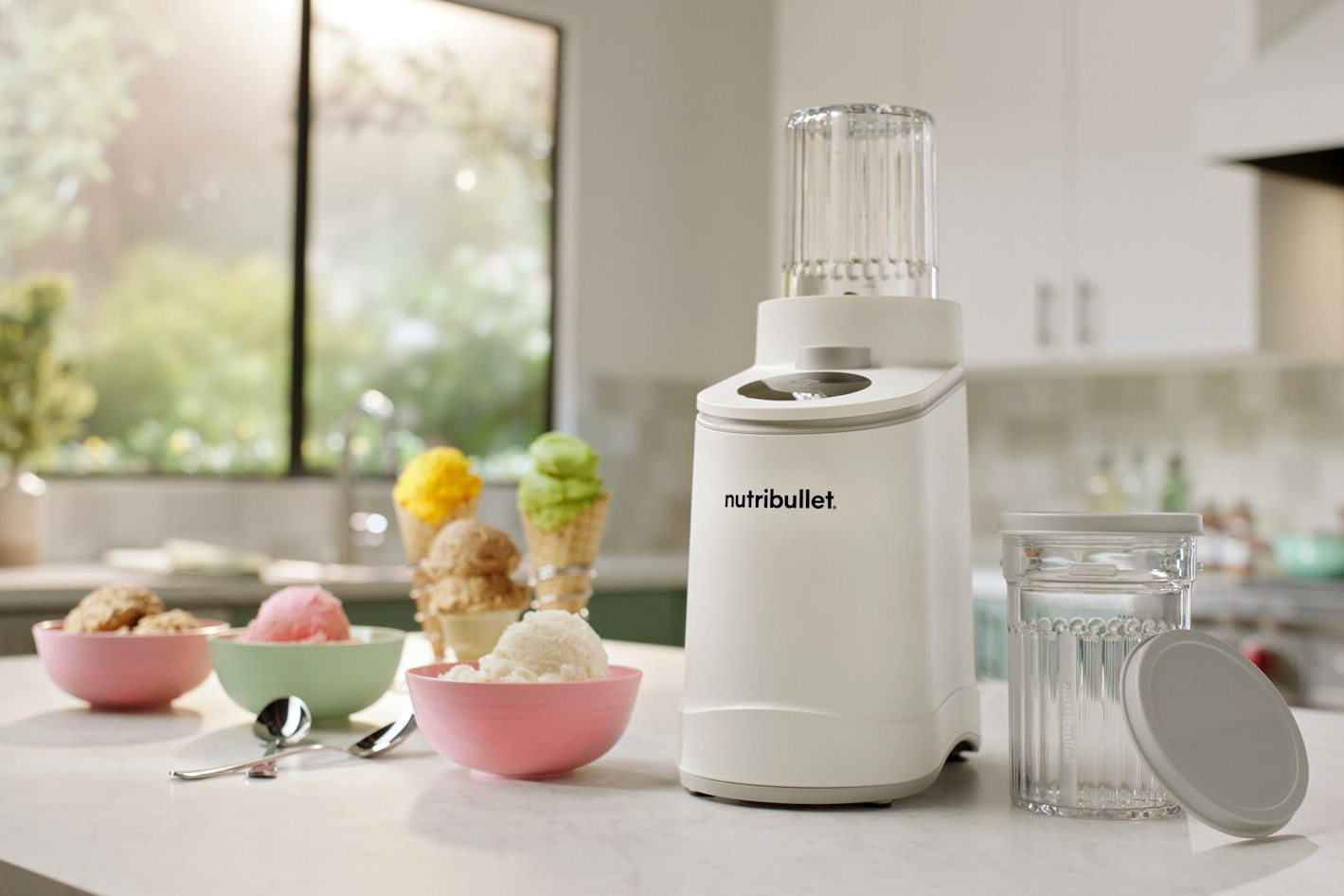 The Nutribullet Chill ice cream maker next to bowls of ice cream on a kitchen counter.