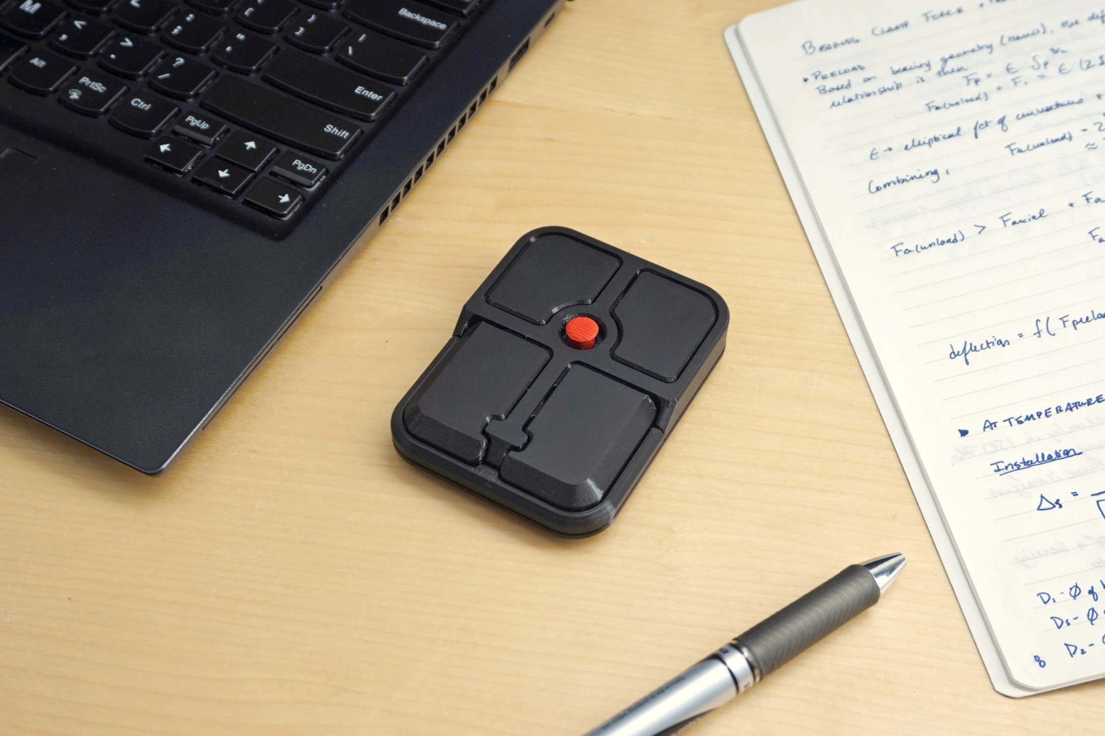 The Ploopy Bean mouse next to a laptop, pen, and papers on a wooden desk.
