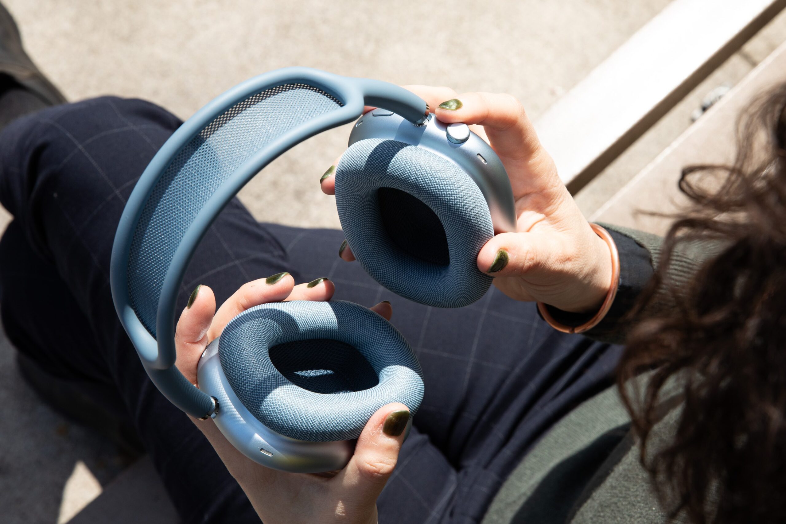 A person holding a pair of blue AirPods Max 2 on a park bench.