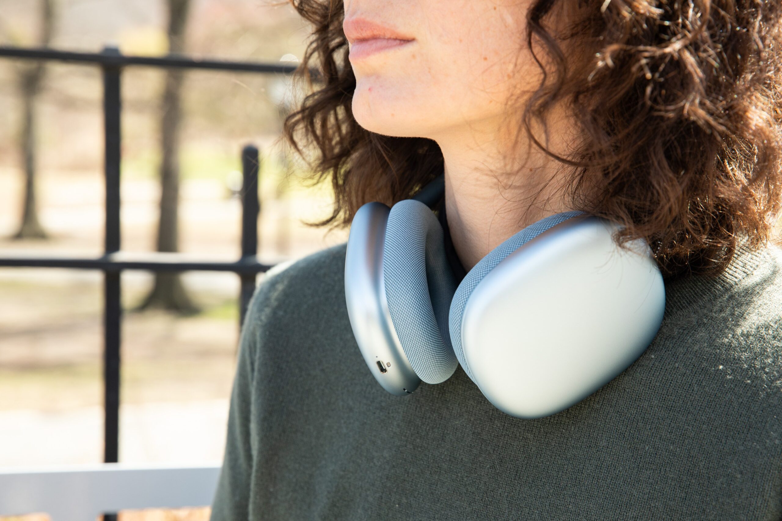 The blue Apple AirPods Max 2 around a person’s neck while outside.