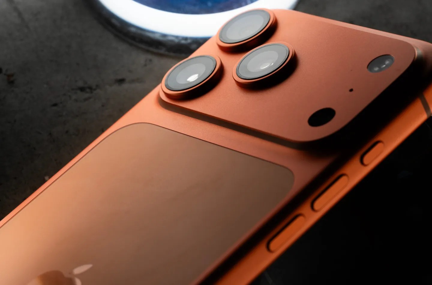 Orange iPhone 17 Pro camera hump against a dark back ground.
