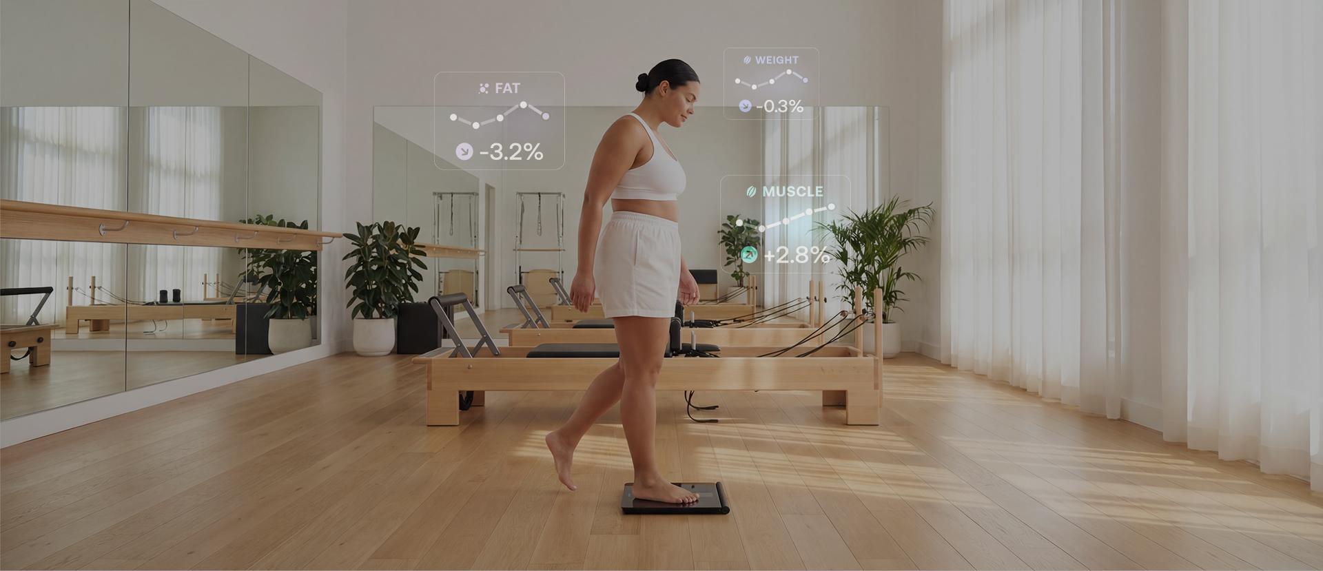 Woman dressed in a white outfit in a modern looking room steps on a scale. in the background there are transparent numbers showing body composition metrics like muscle and body fat.