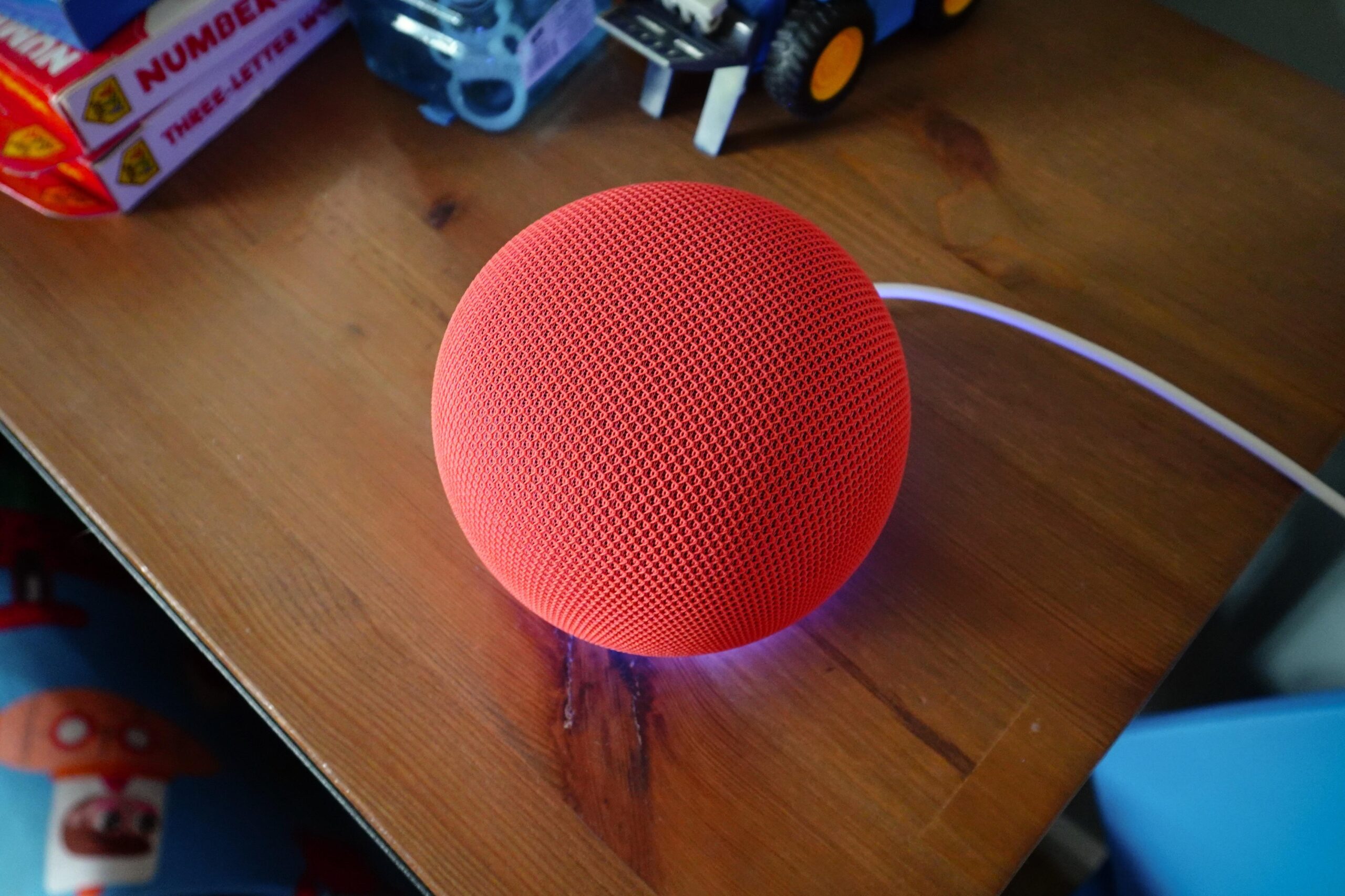 A photo of a round, red smart speaker on a table.