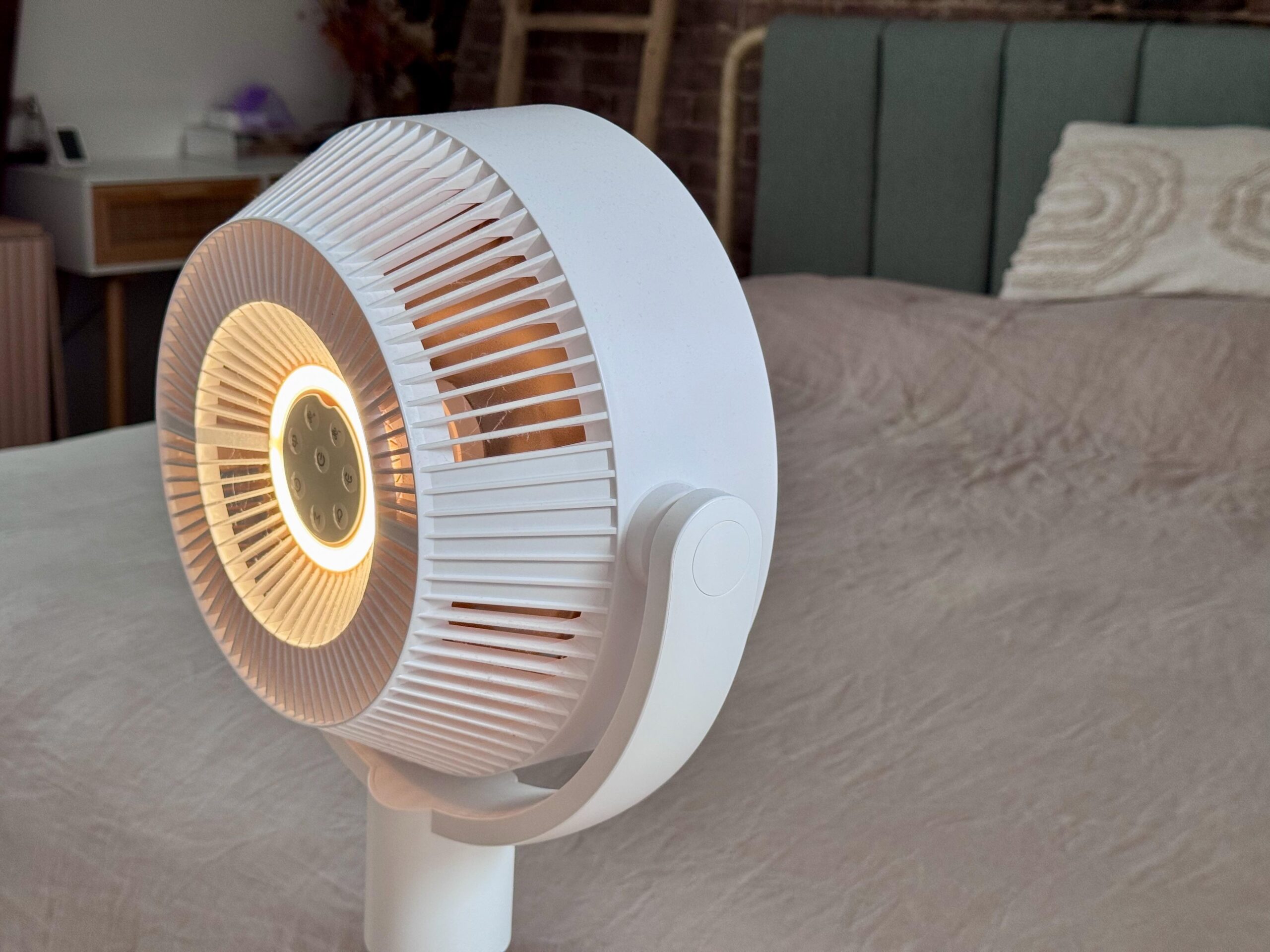 The fan, with a light-ring glowing in the center of the back, pointed at a bed.