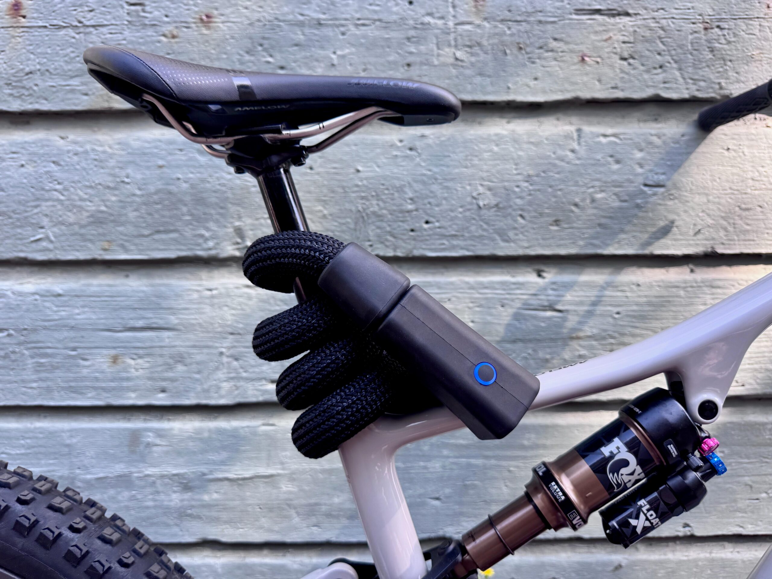 The bike lock wrapped around the seat post of an e-bike with a rear shock, saddle, and the top of the knobby rear wheel in view.