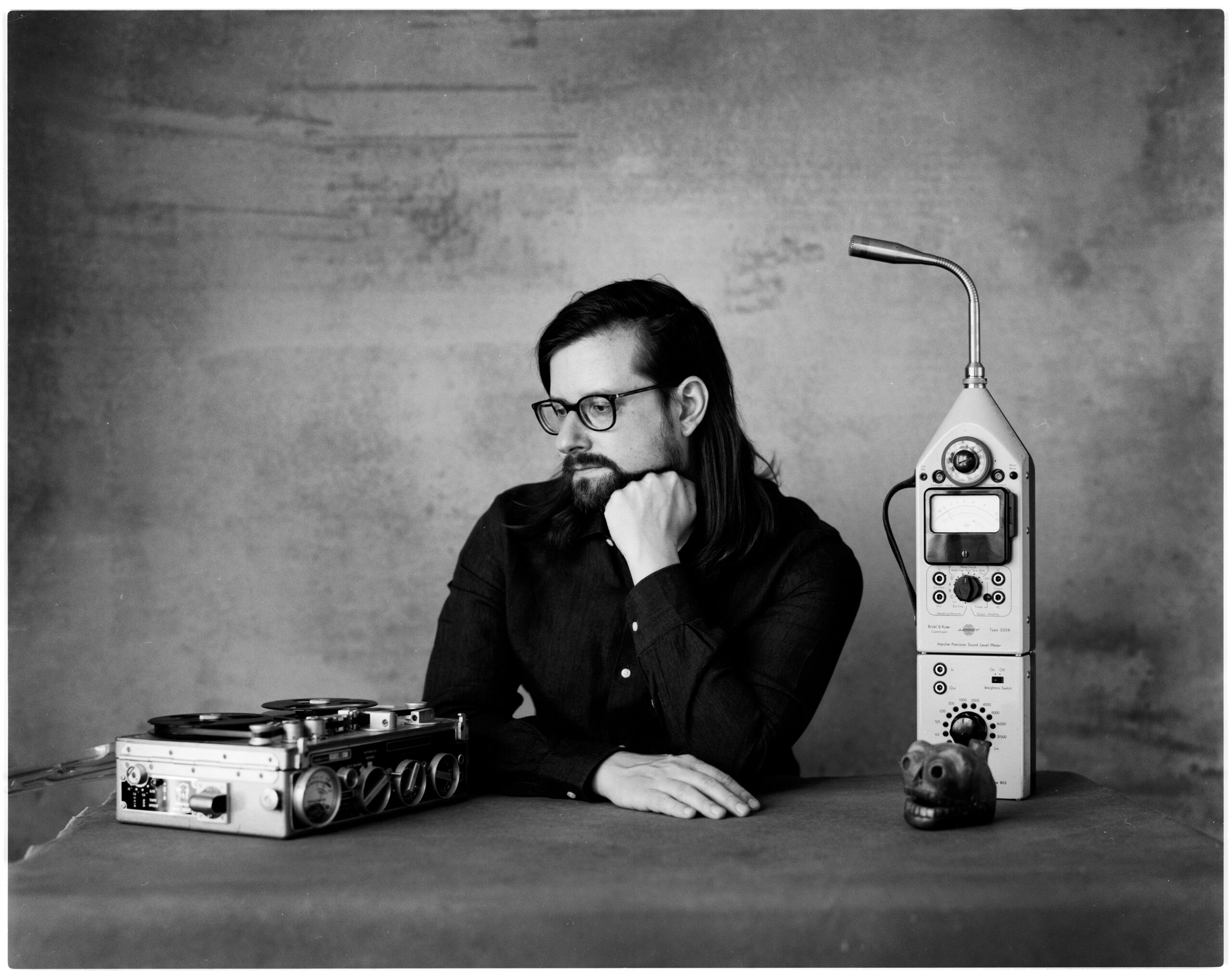 A black and white photo of Hainbach at a table with two pieces of scientific equipment that he uses to make music.